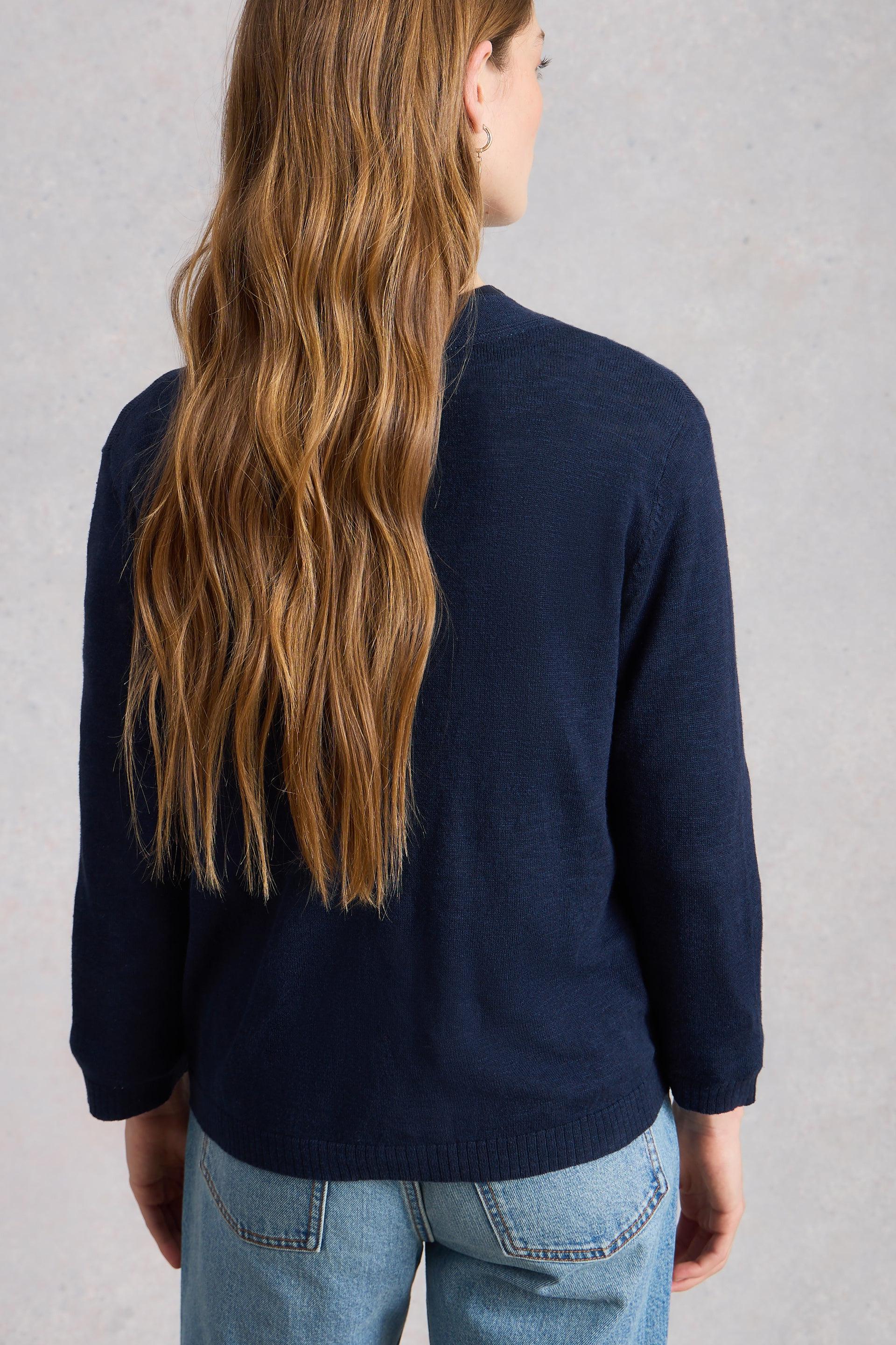 Person wearing a navy organic cotton cardigan and blue jeans against a gray background