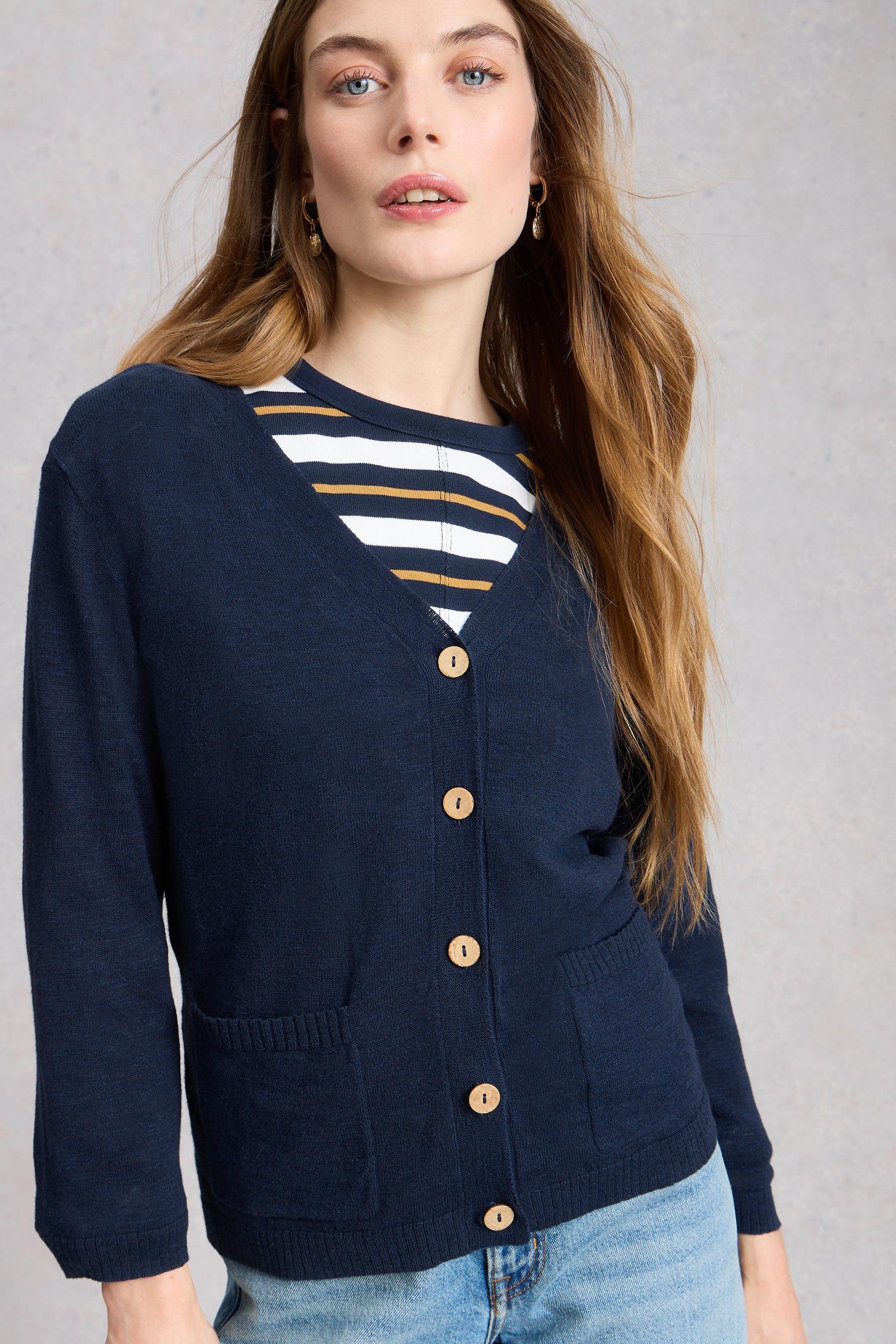 Woman wearing a navy organic cotton cardigan over a striped shirt with a plain background