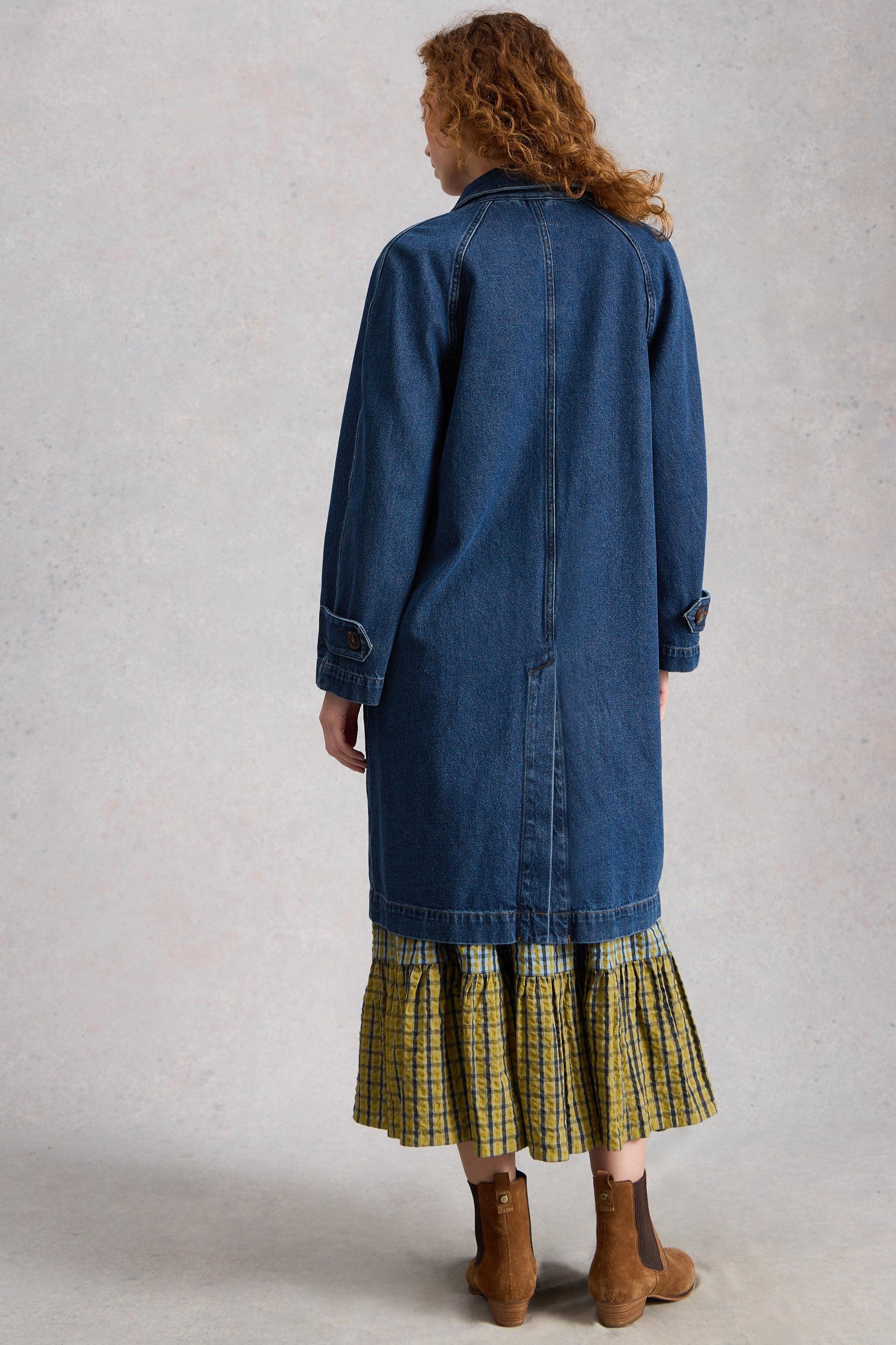 Person wearing a long denim coat over a plaid skirt on a plain background