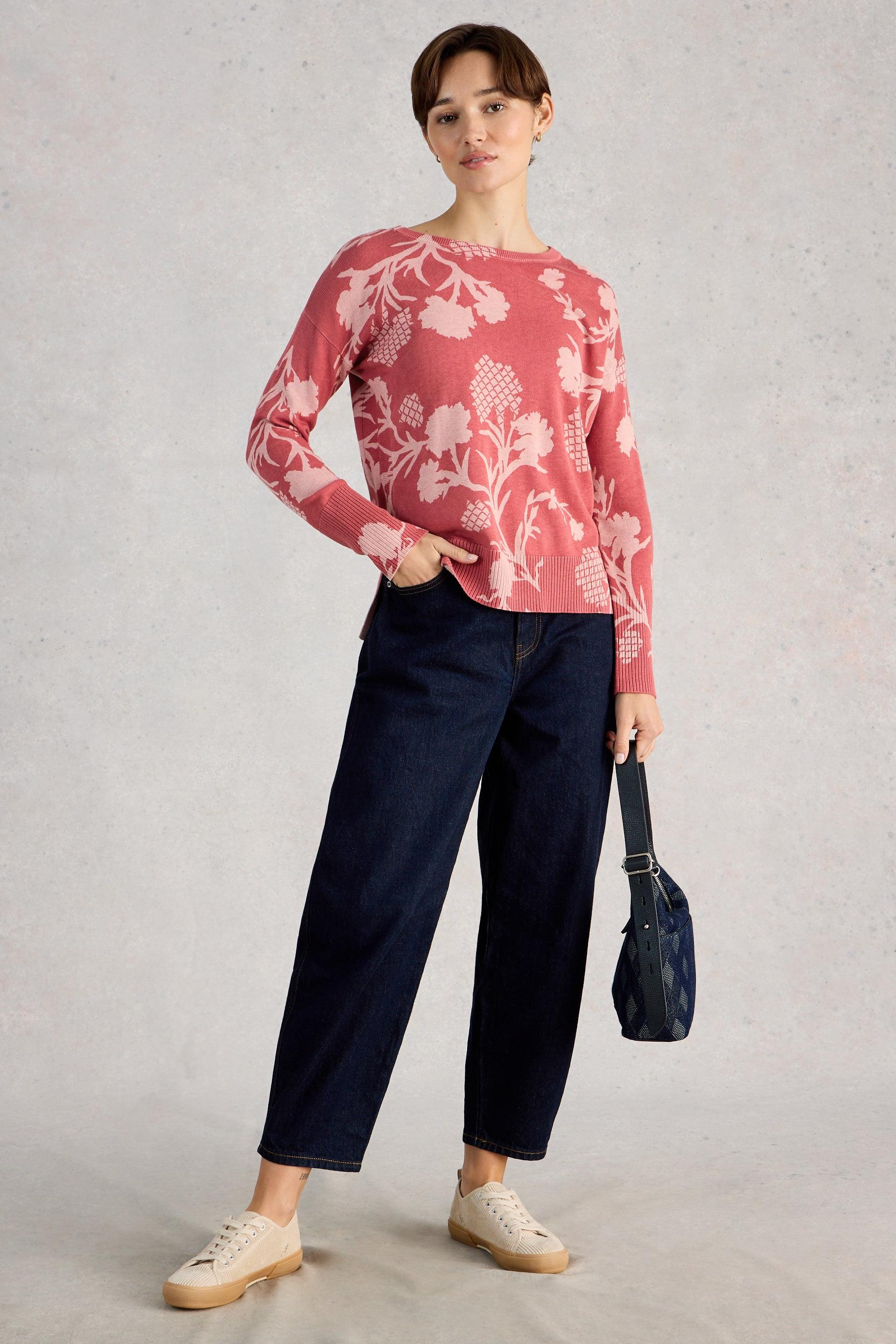 Woman wearing a floral organic cotton and dark jeans, holding a black handbag on a light gray background