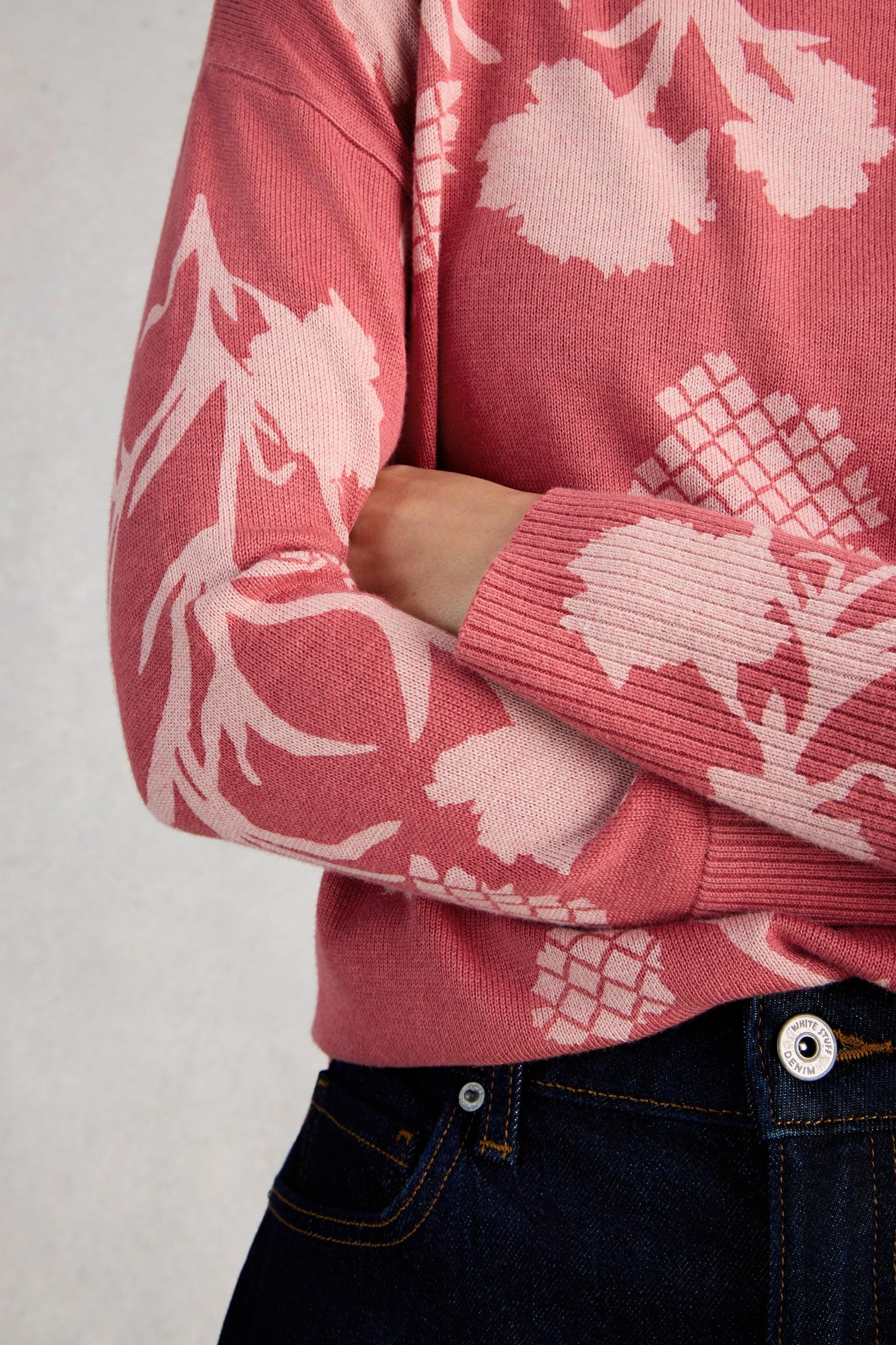 Close-up of a pink organic cotton sweater with white floral patterns on a plain background