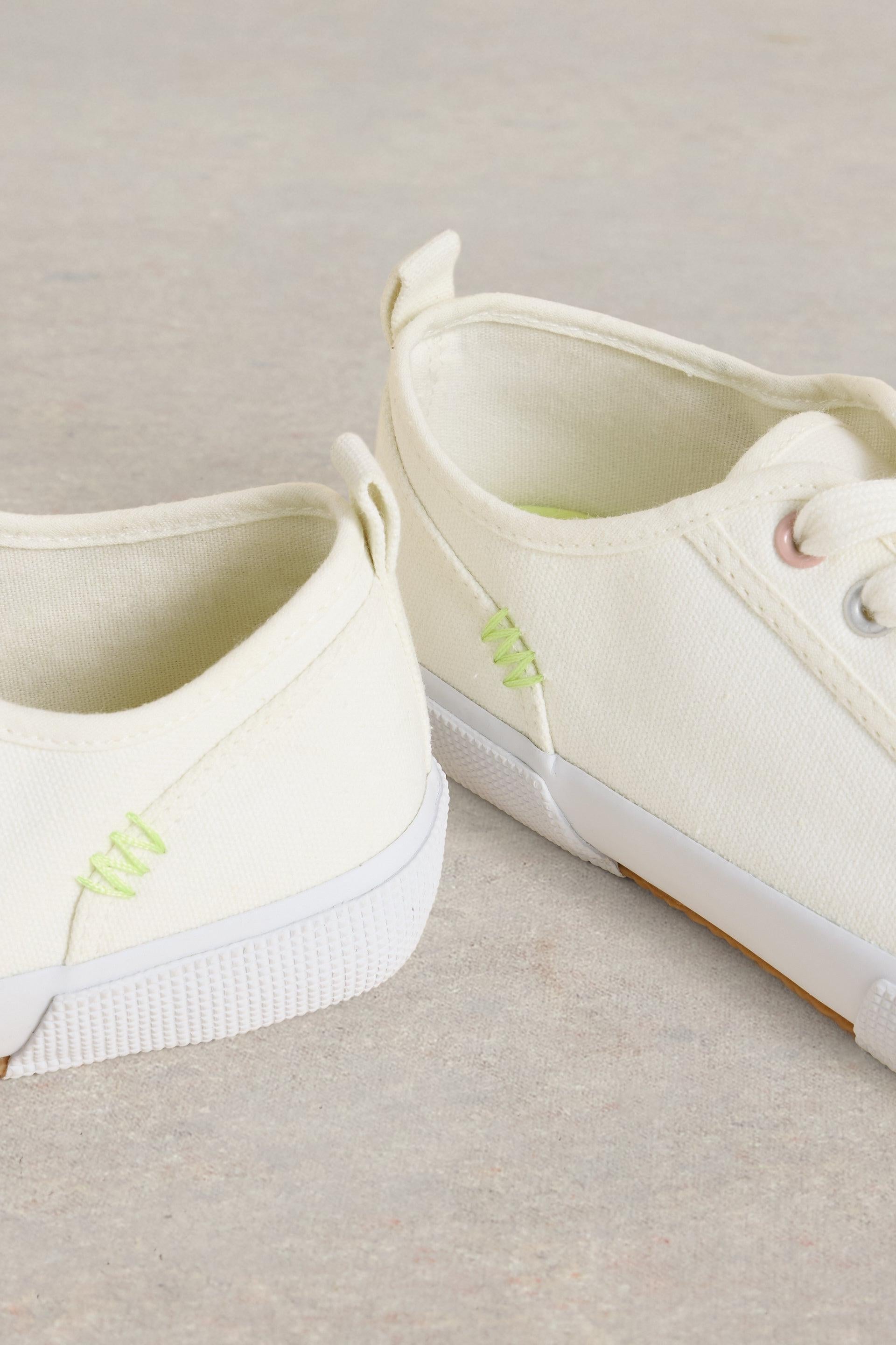 Close up of lime stitching on the side of canvas trainers.