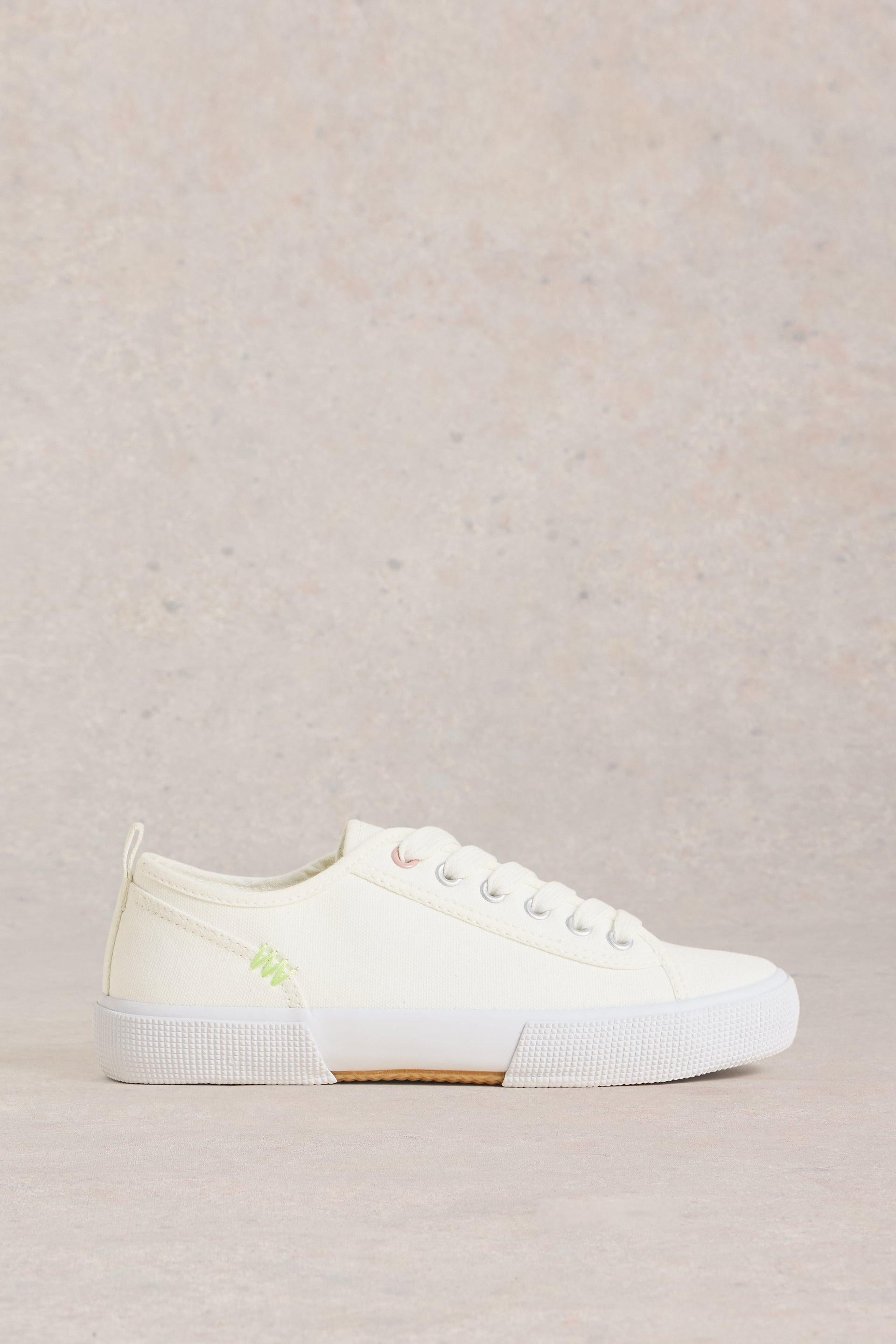 White canvas trainers with lime stitching on the side.