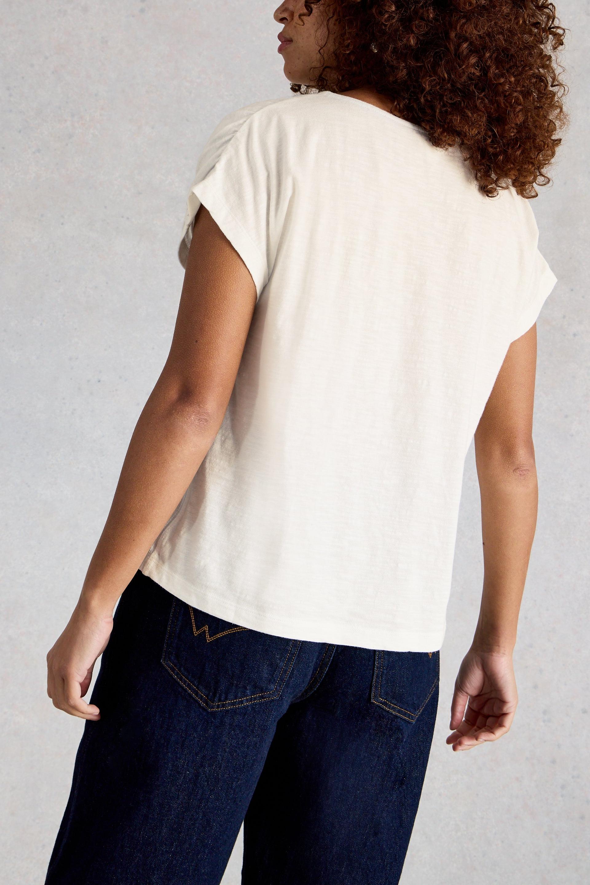 Person wearing a white t-shirt and dark jeans against a plain background