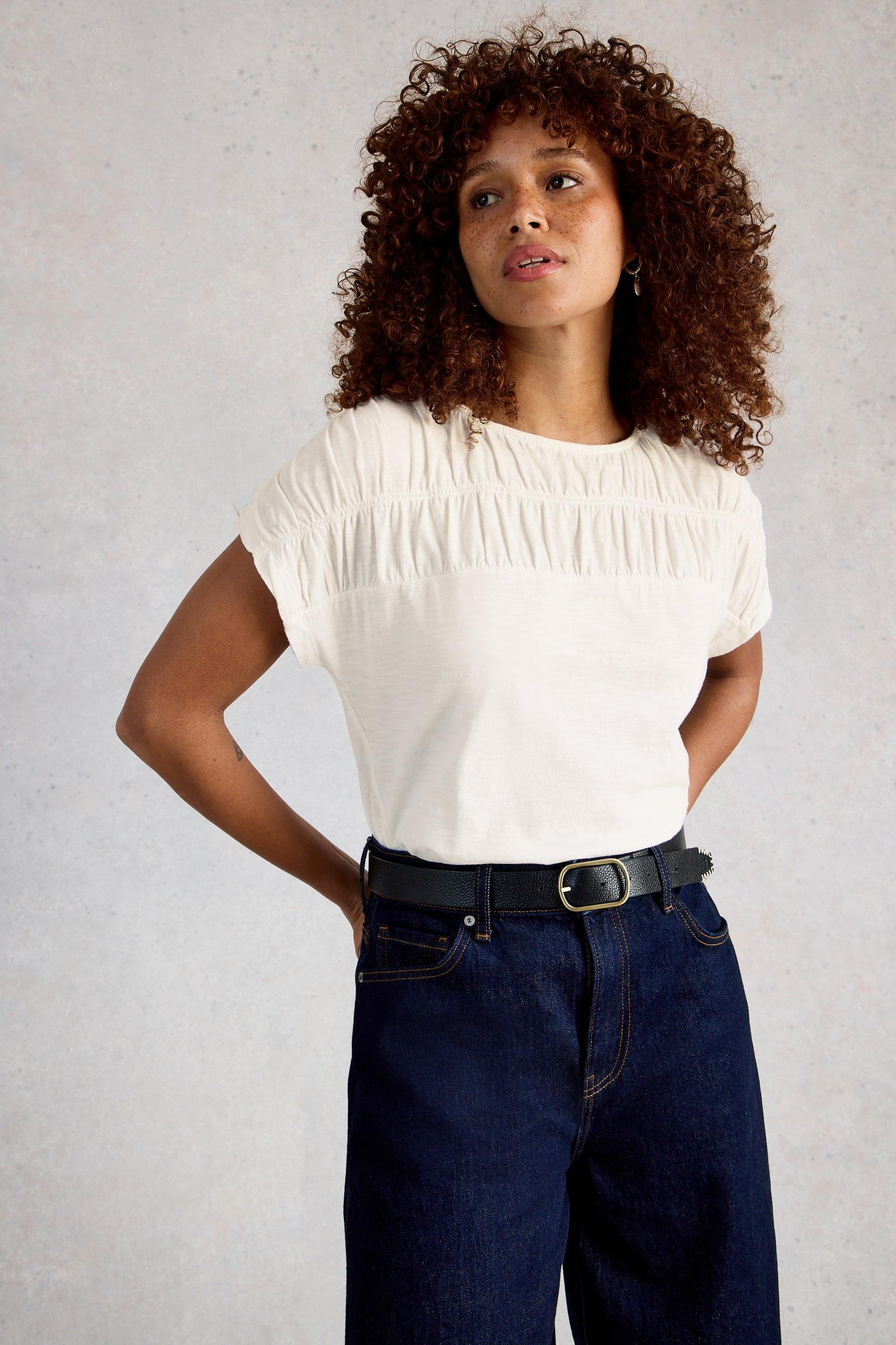 Woman wearing a white organic cotton blouse and dark blue jeans against a plain background
