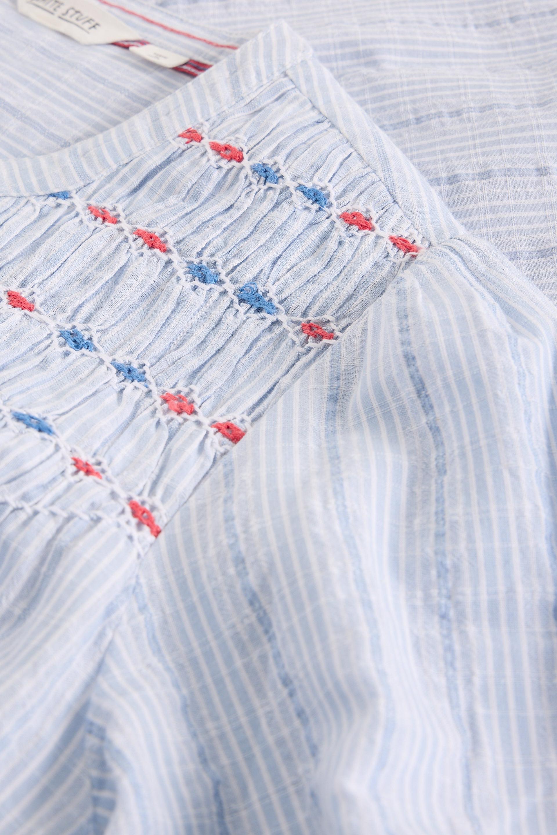 Close-up of a blue blouse with blue and red floral embroidery on a white background