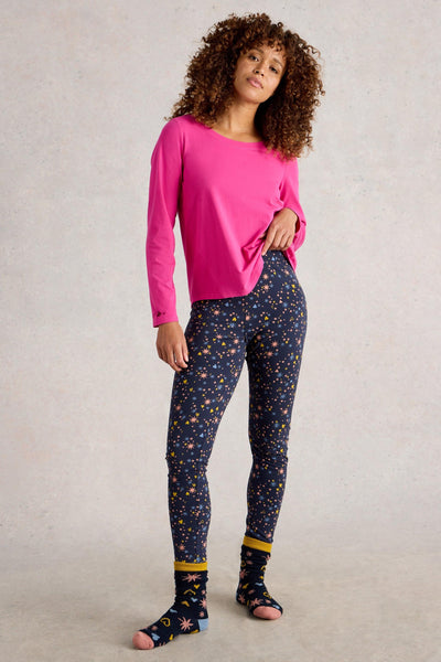 Woman wearing a pink organic cotton top and navy pyjama bottoms with star pattern on a plain background