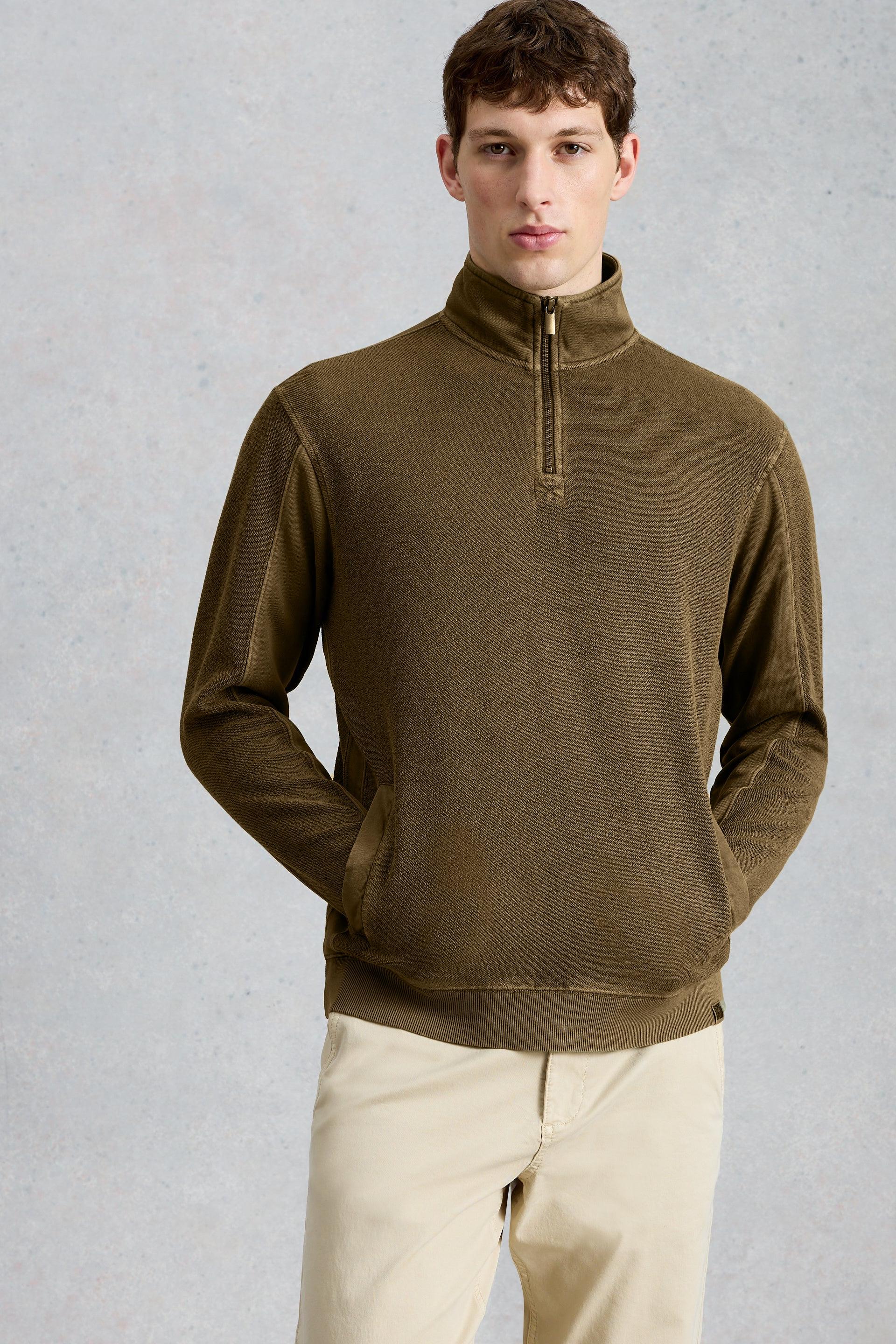 Man wearing a green half-zip pullover against a gray background