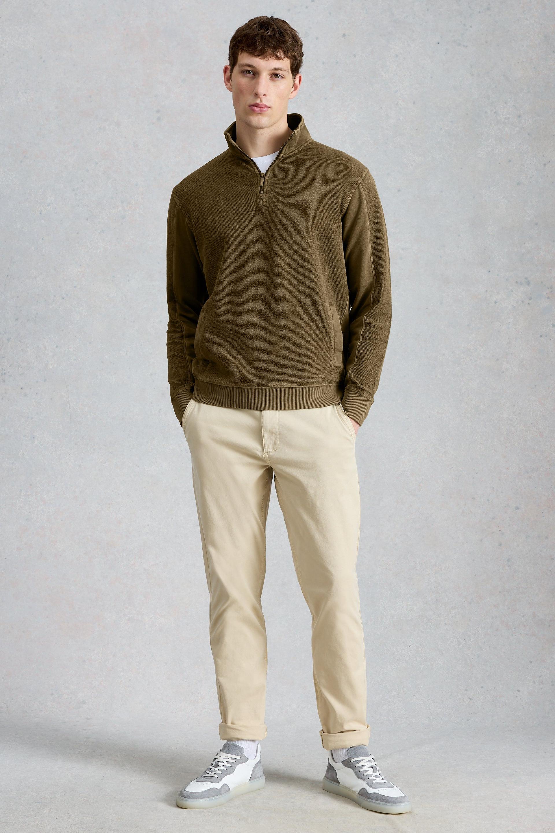 Man wearing a green organic cotton pullover and beige pants on a gray background