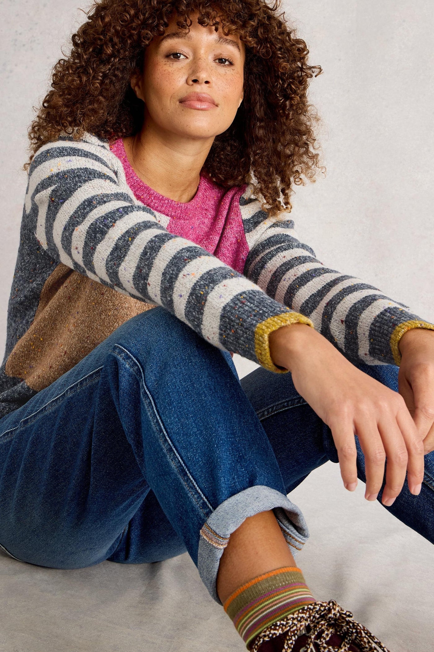 Model sitting wearing organic cotton knit jumper showing striped sleeves
