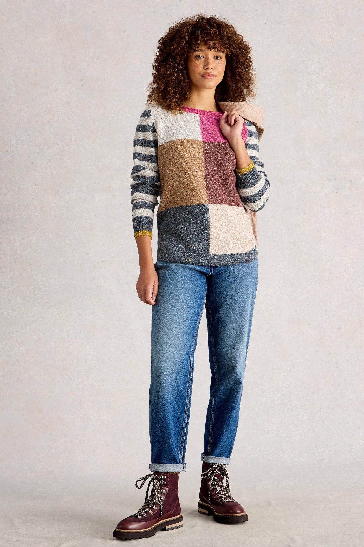 Model wearing multicolour organic cotton knit jumper, styled with straight blue denim jeans and military style boots