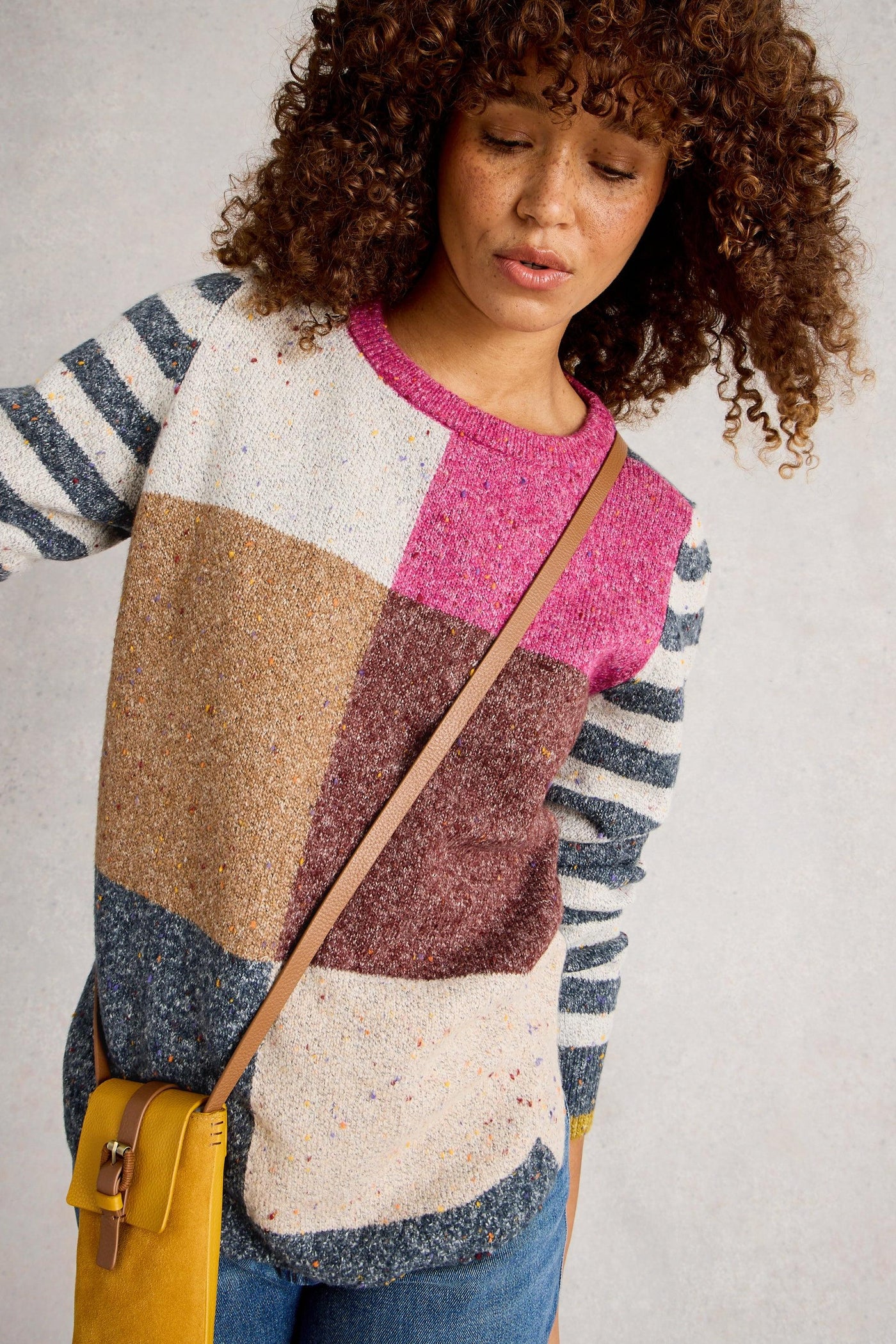 Woman wearing knit jumper with multicoloured squares on the body, white and blue striped sleeves, and pink crew neck