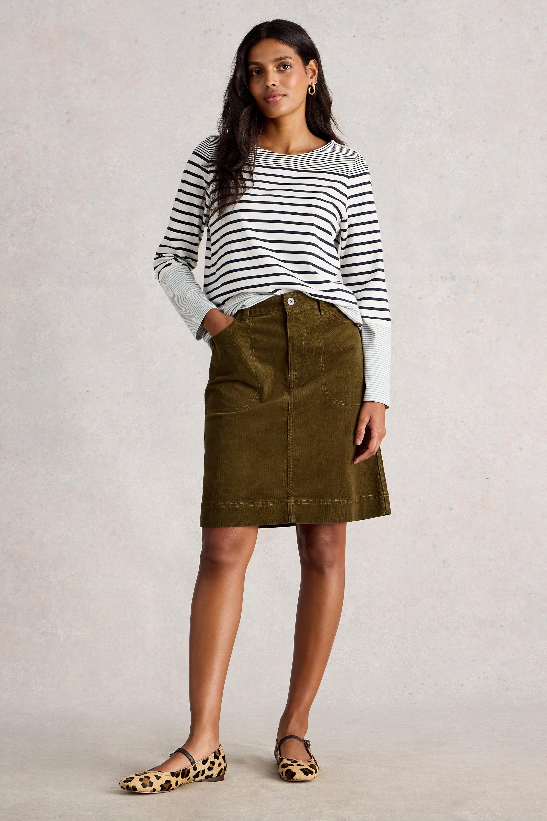 Woman wearing a striped sweater and corduroy skirt against a plain background
