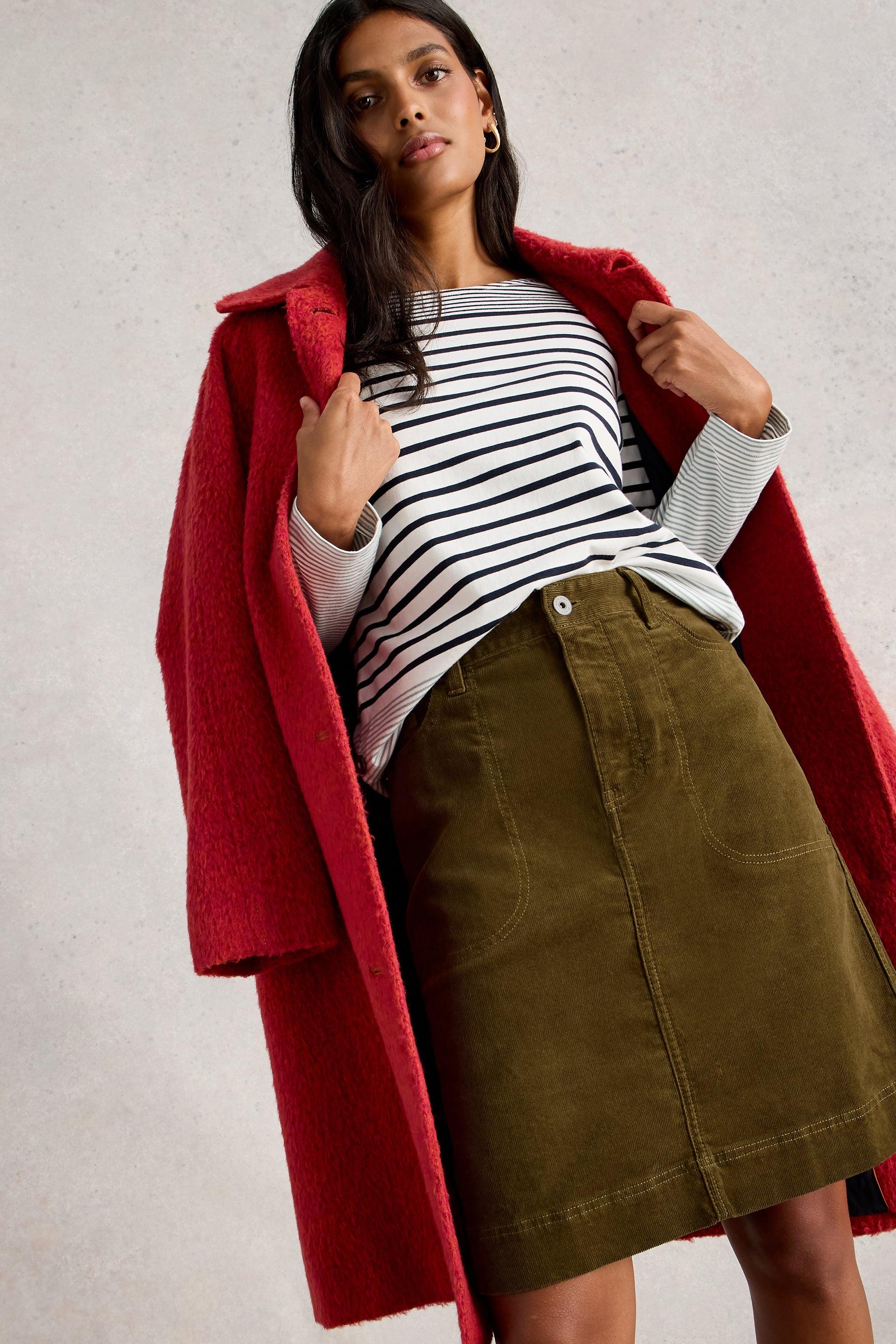 Woman wearing a red coat, striped shirt, and green skirt on a plain background