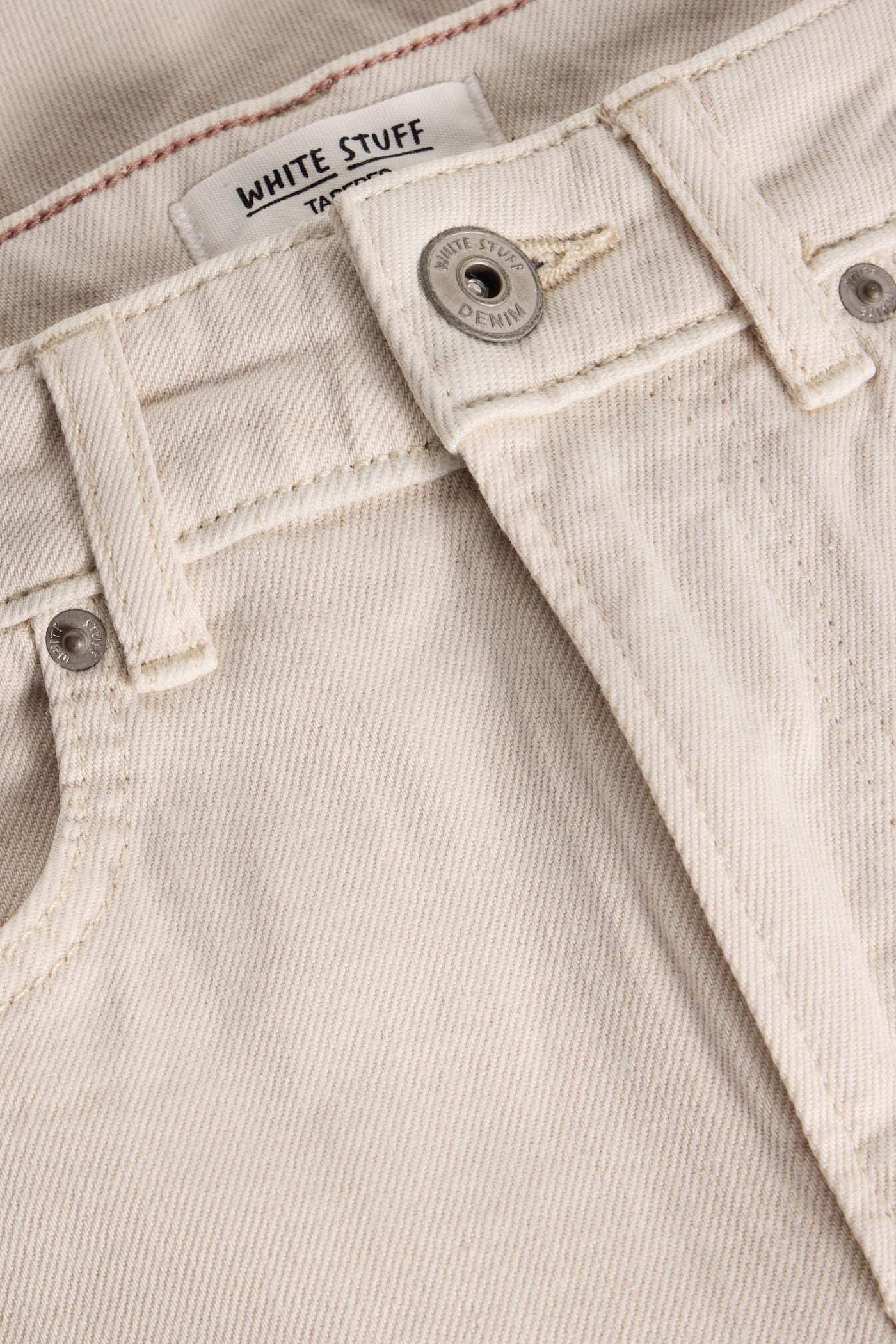 Organic cotton tapered jeans in natural white, folded flat showing hem and button detail