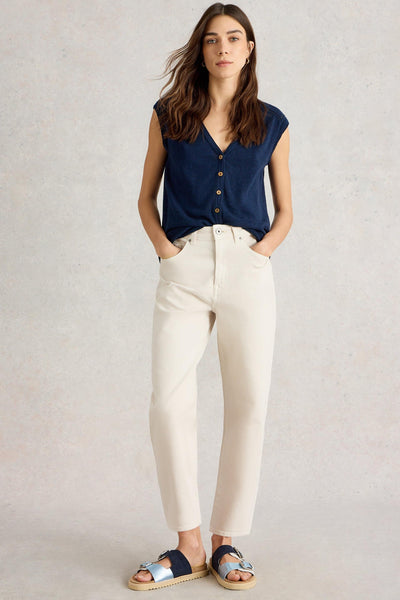 Woman wearing tapered ankle-length jeans in natural white organic cotton, styled with a navy sleeveless top and sandals