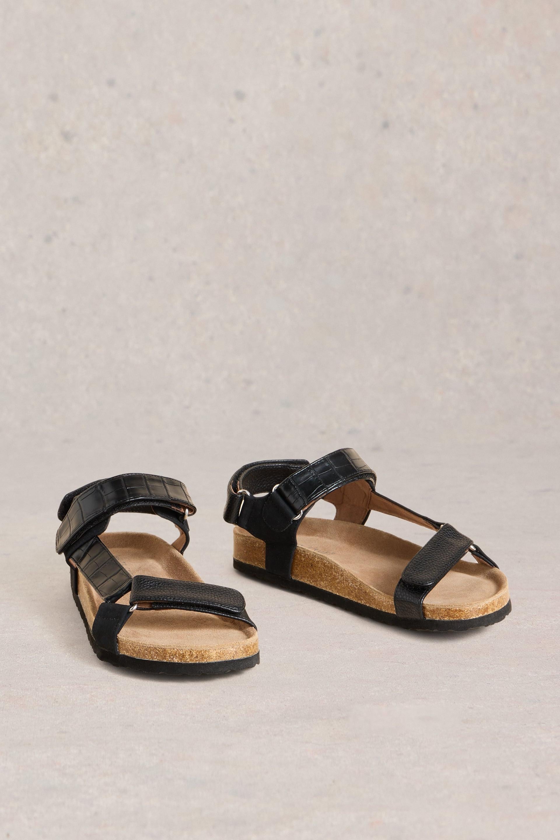 Black leather strappy sandals on a neutral background.