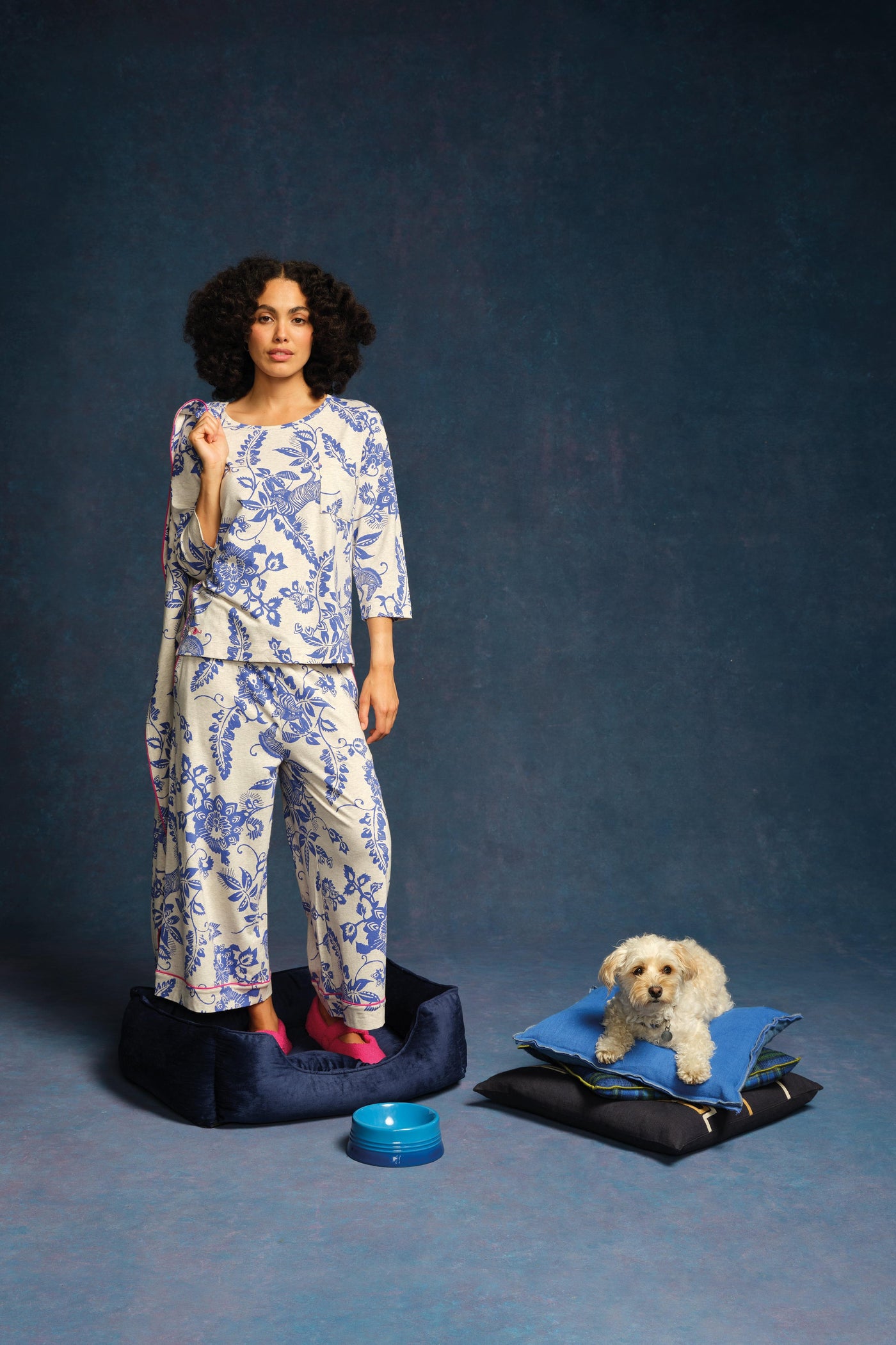 Woman in blue and white floral pyjamas standing next to a dog on a blue background