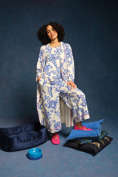 Woman in a blue and white floral outfit sitting on a blue background with pillows and a dog bed.