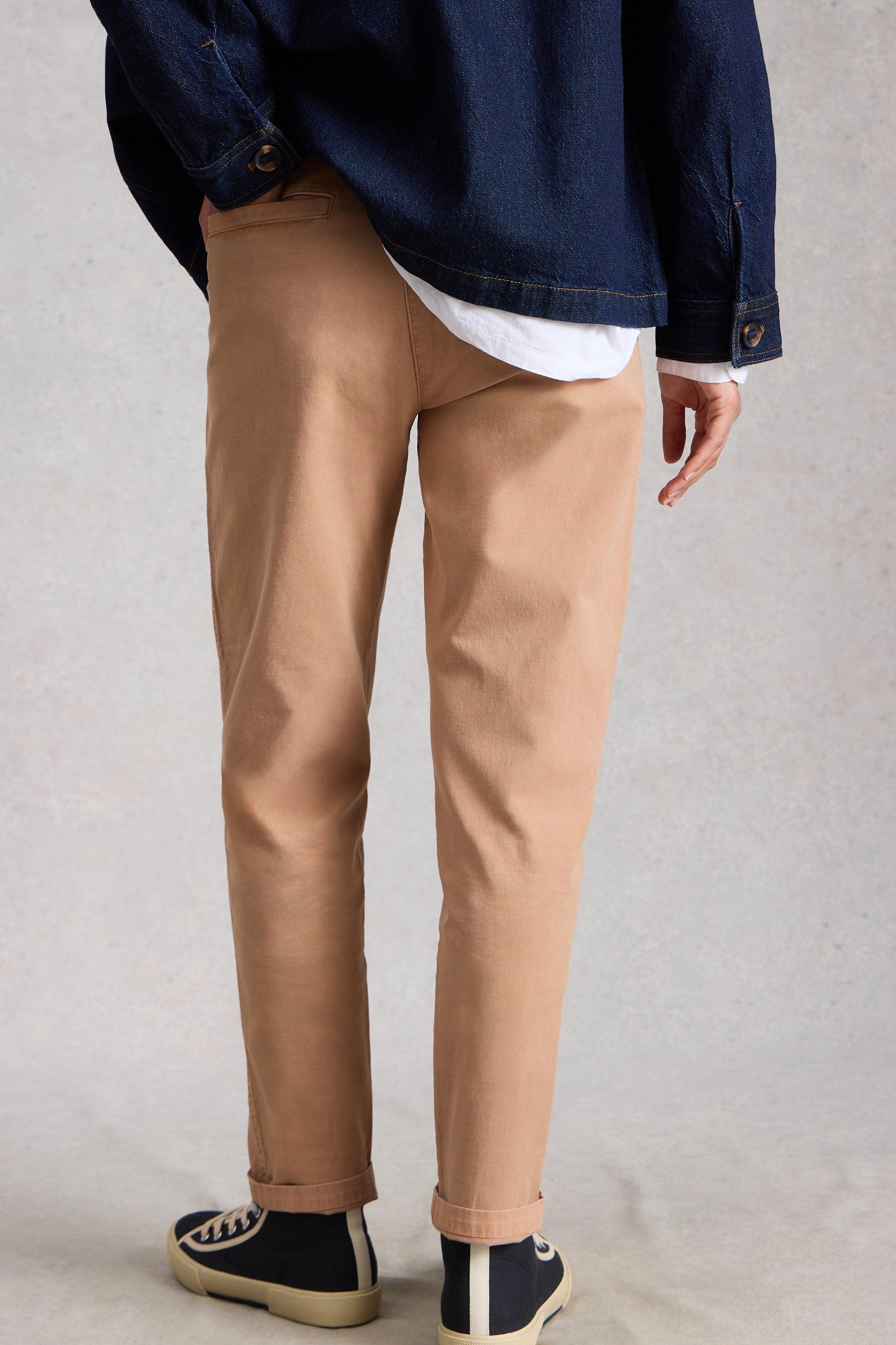Person wearing tan pants and a dark jacket on a plain background