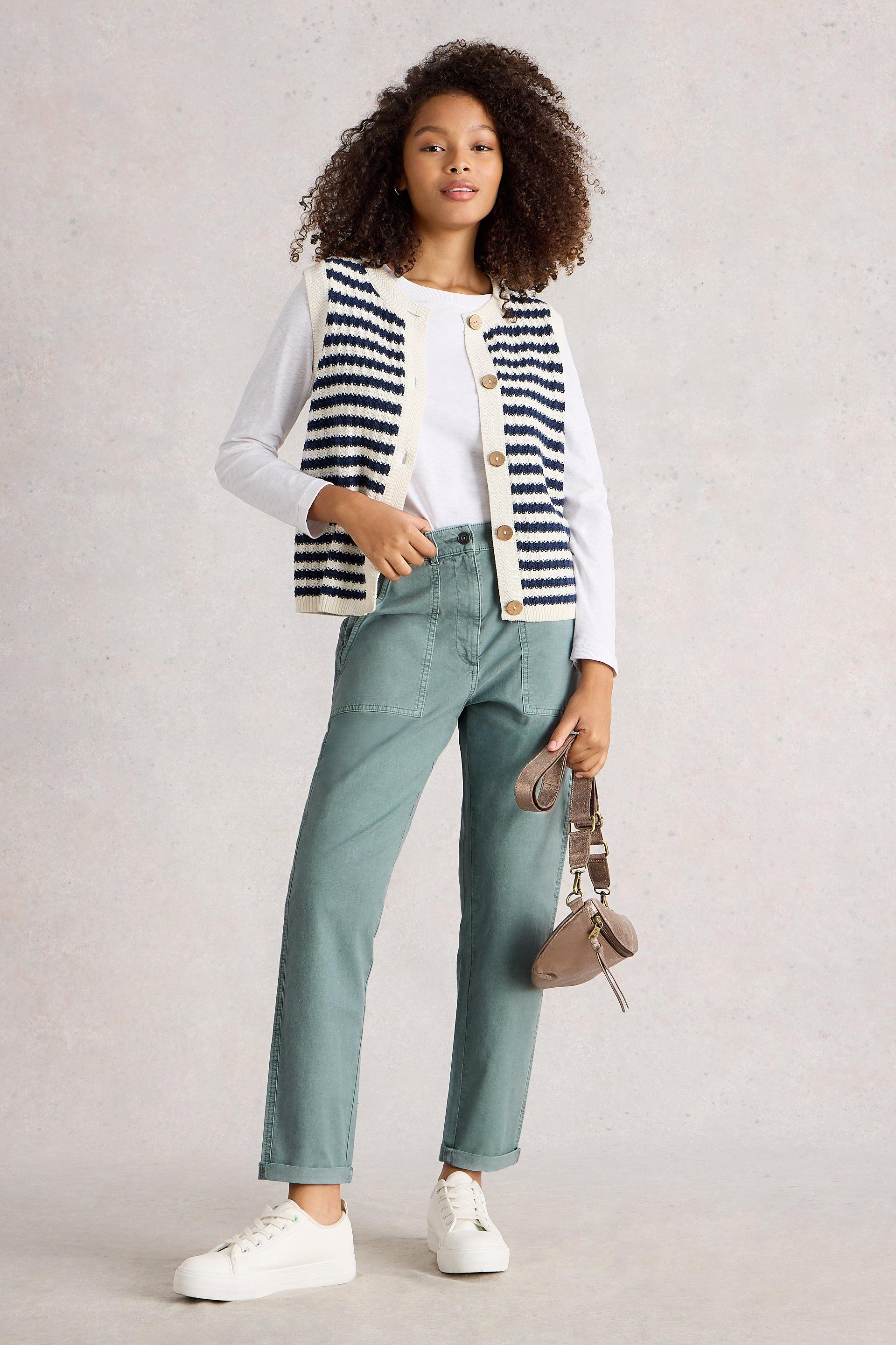 Woman wearing a striped cardigan, white shirt, blue tapered pants, and white sneakers on a light background