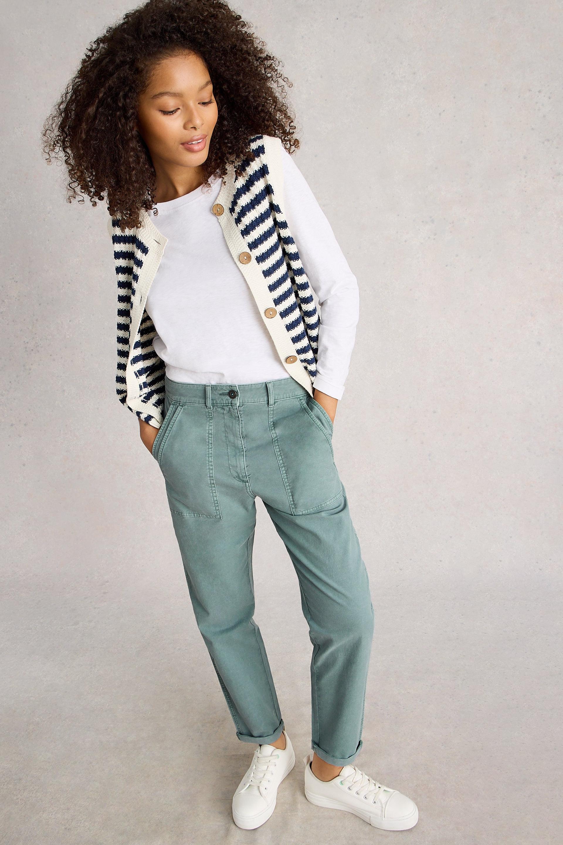 Woman wearing a striped cardigan, white shirt, blue tapered chinos, and white sneakers on a gray background