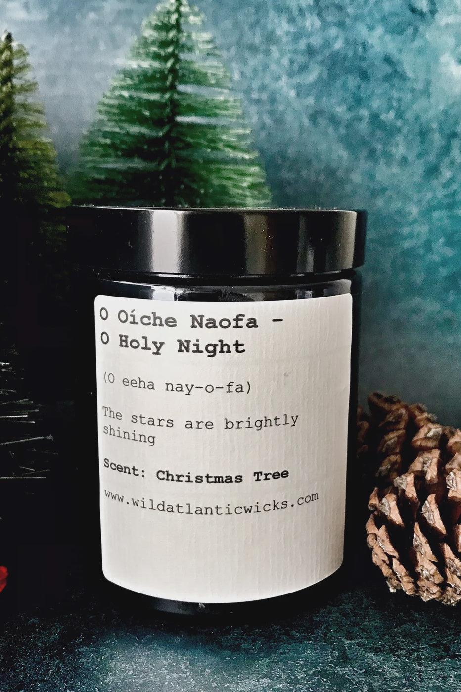 Candle with a label in a festive setting with trees and a pine cone.
