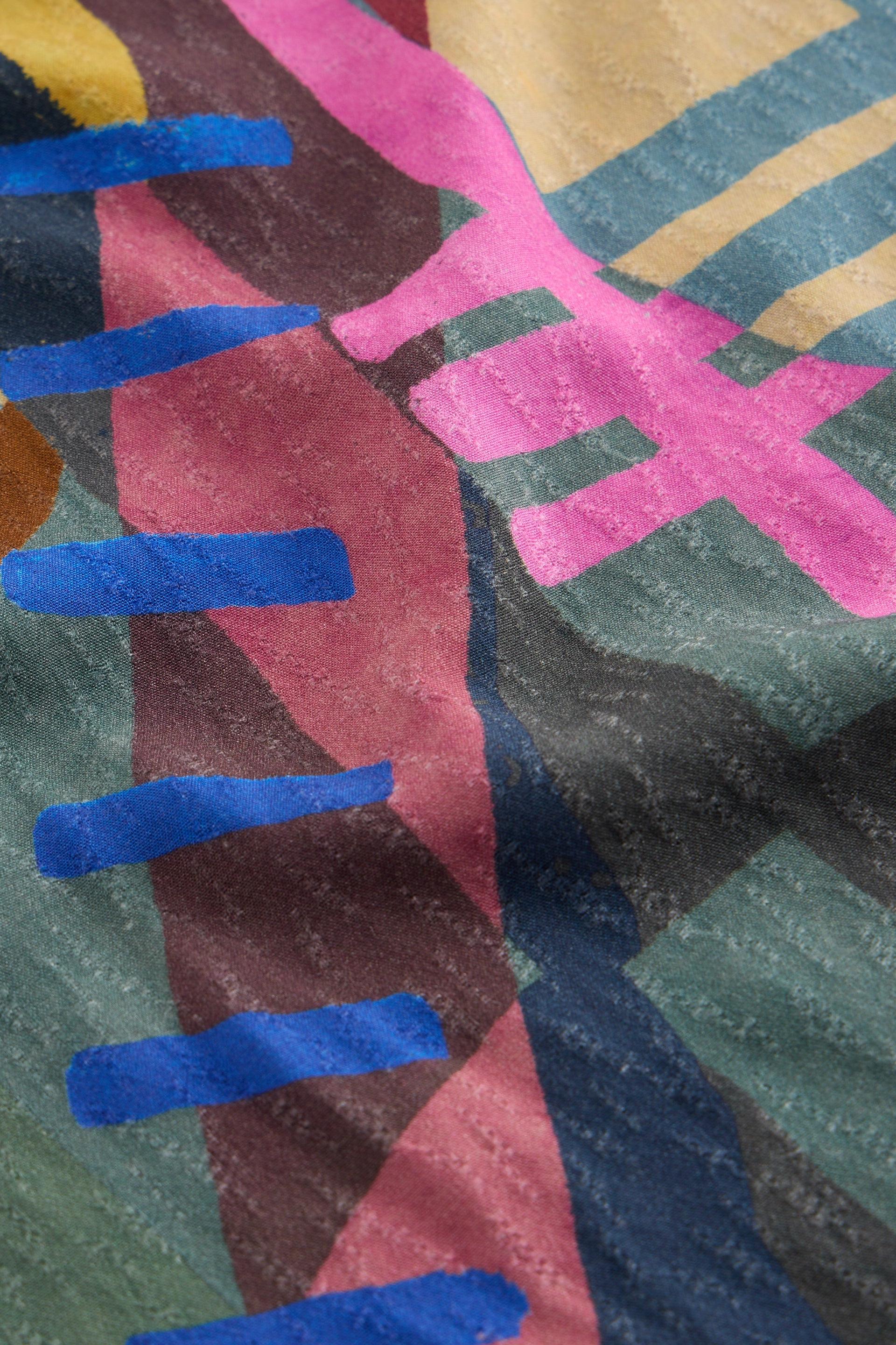 Close-up of pleated Ecovero fabric featuring a colorful abstract pattern with geometric shapes.