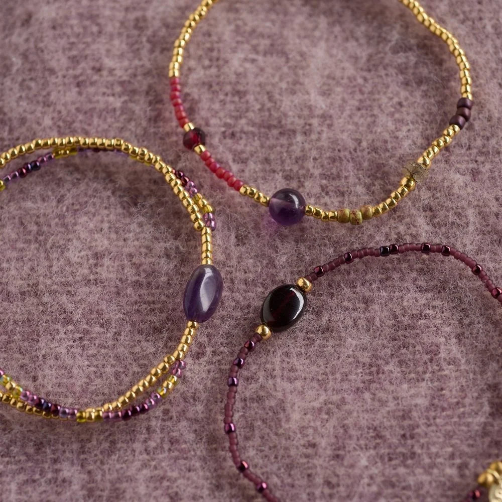 Three handmade beaded bracelets featuring amethyst gemstones on a textured purple wool background.