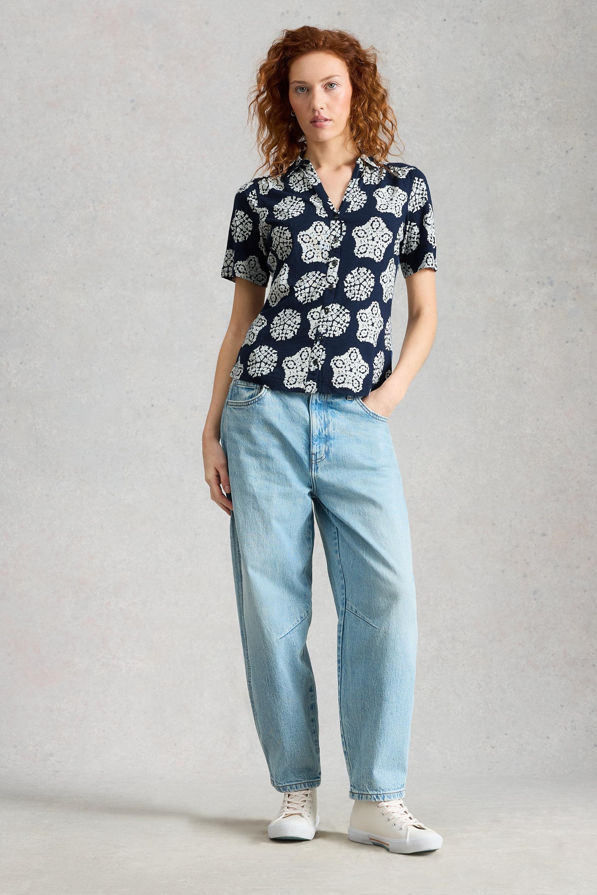 Woman wearing a patterned organic cotton shirt and jeans on a plain background