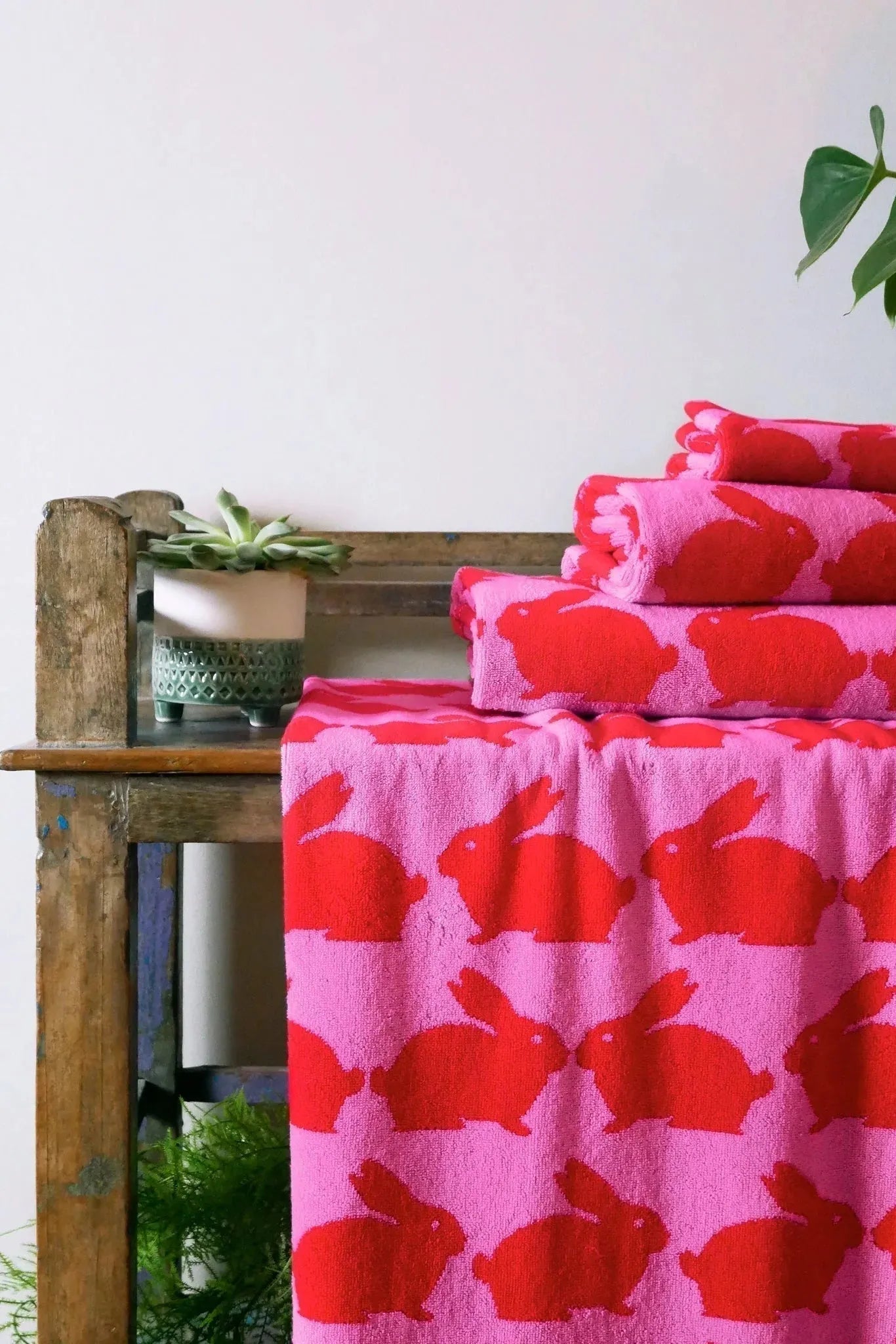 Pink towels with red bunny pattern on a wooden table against a white wall.