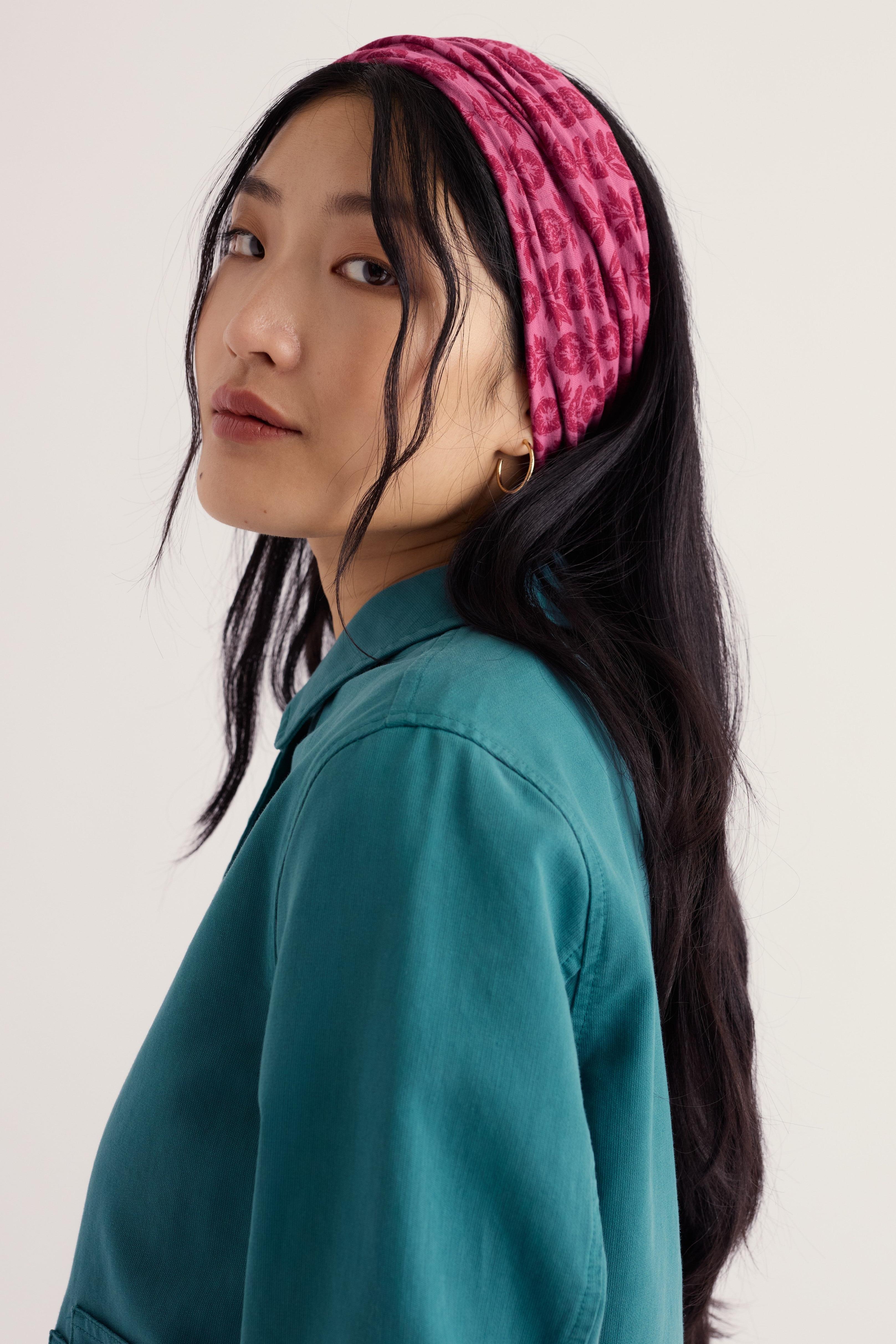 A woman wearing a textured pink and red patterned headband and a teal button-up shirt, shown in a side-profile view against a plain light background.
