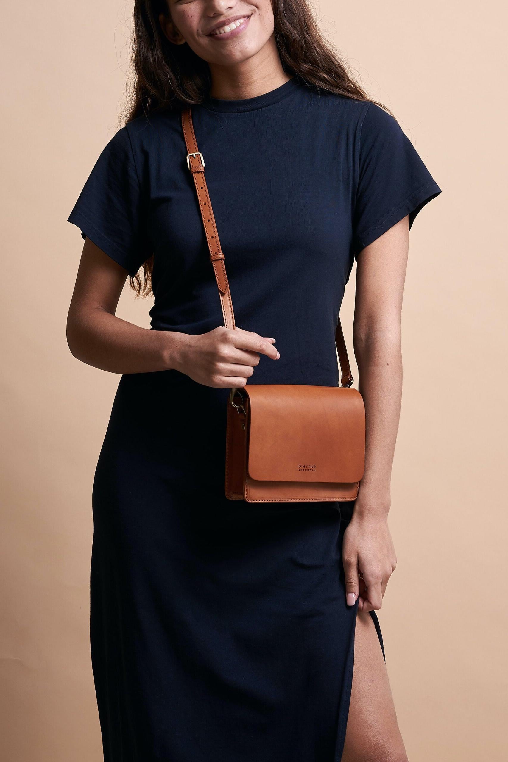 Woman holding a brown leather bag against a beige background