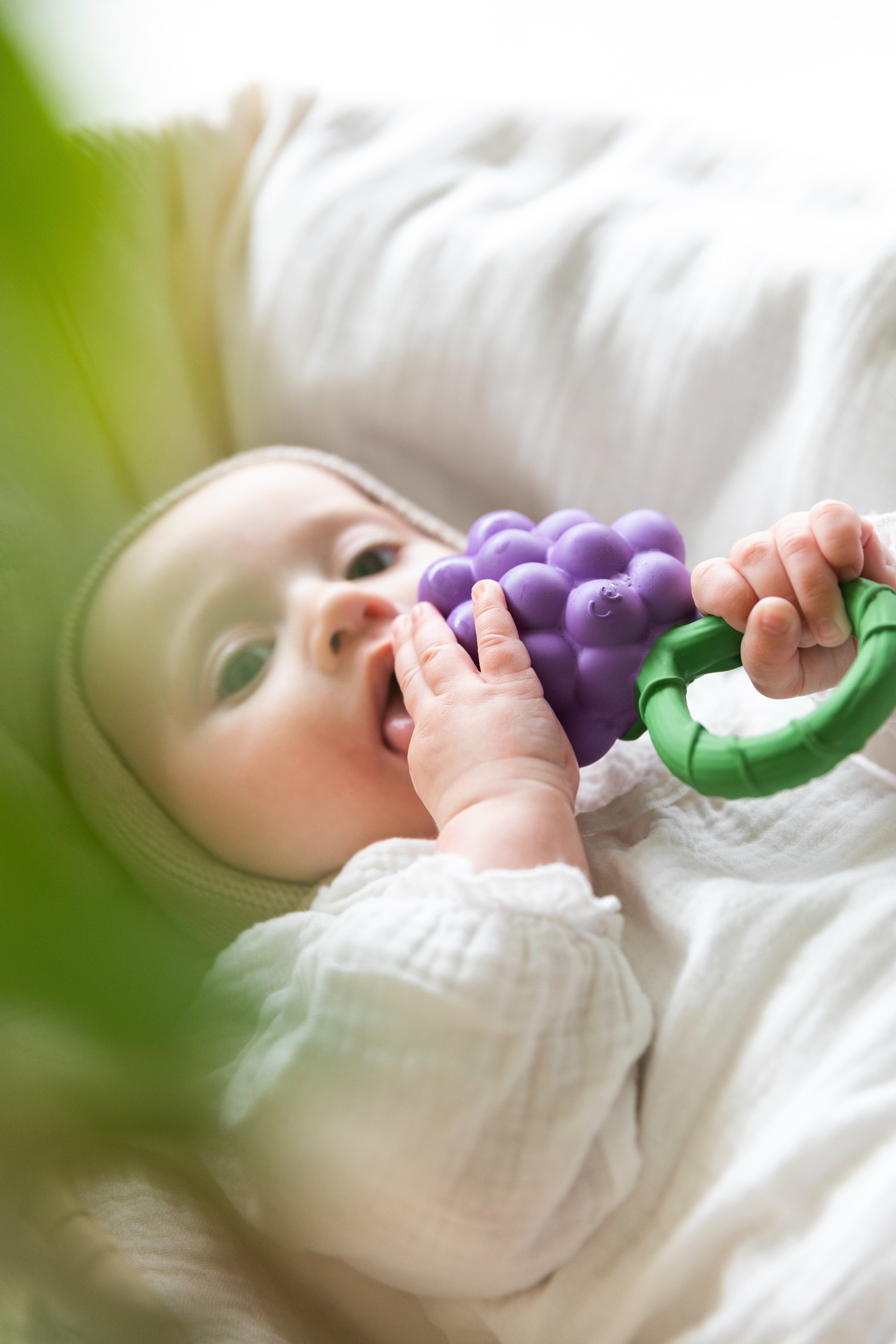 Baby holding a handcrafted grape-shaped baby rattle and teether