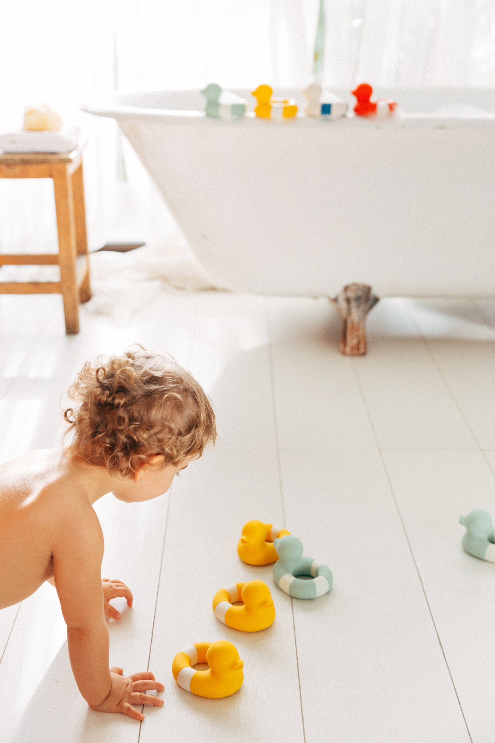 Child playing with natural rubber bath toys on a bathroom floor next to a bathtub.