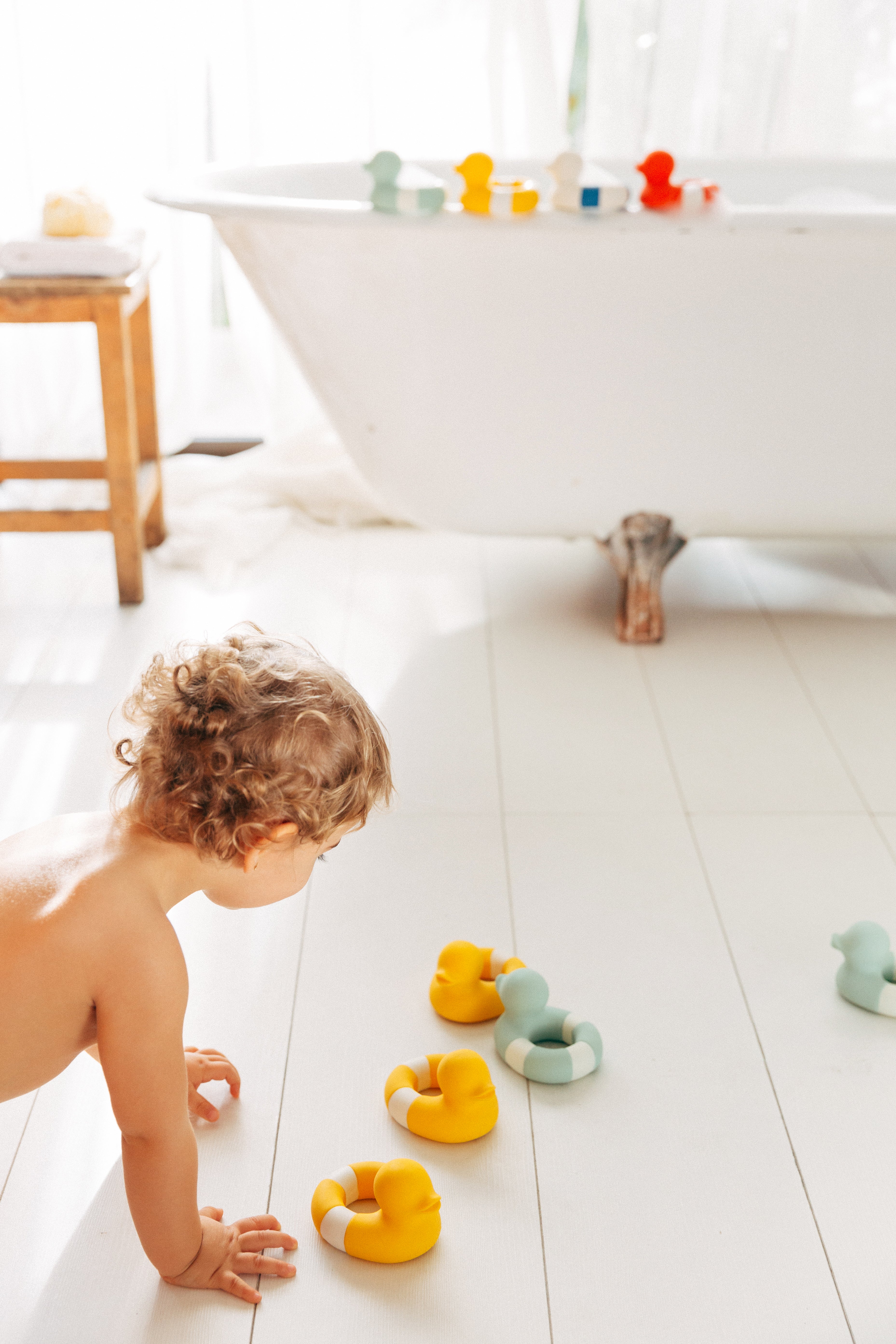 Child playing with natural rubber bath toys on a bathroom floor next to a bathtub.