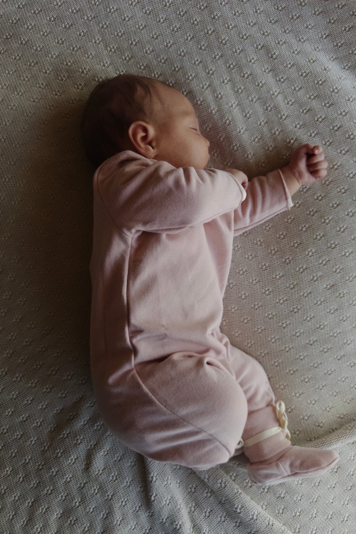 Newborn baby in a pink onesie lying on a textured surface
