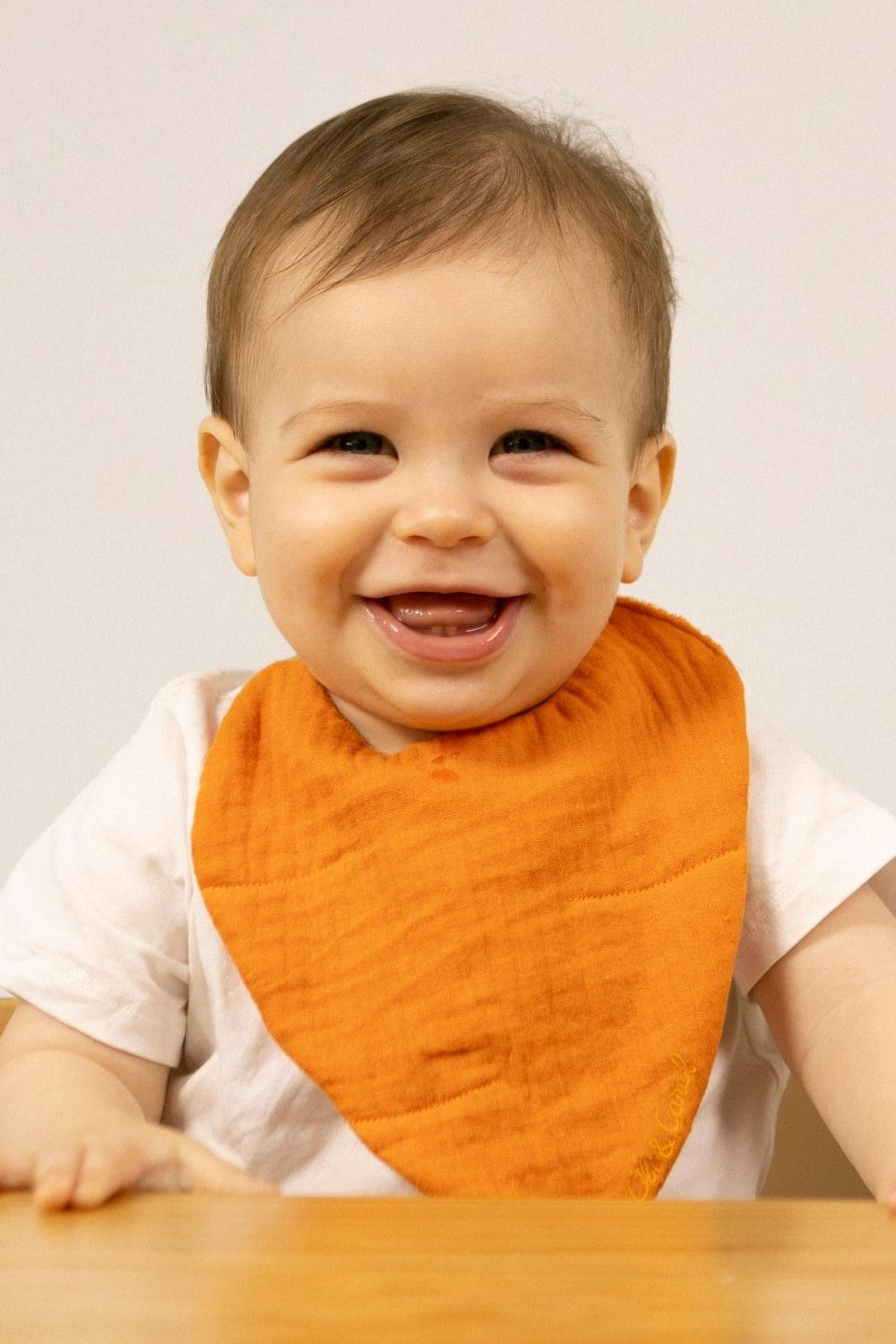 Baby wearing an orange organic cotton bib against a plain background
