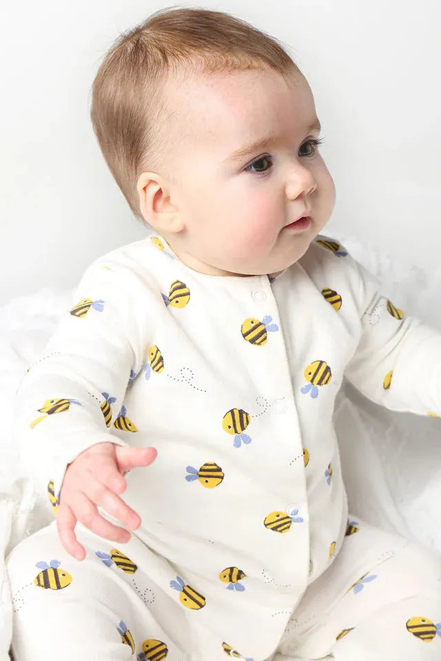 A cute baby wearing an organic cotton Frugi onesie with a playful bumblebee print