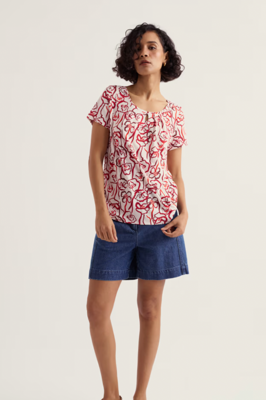 Woman wearing a red and white patterned top with blue shorts on a light background