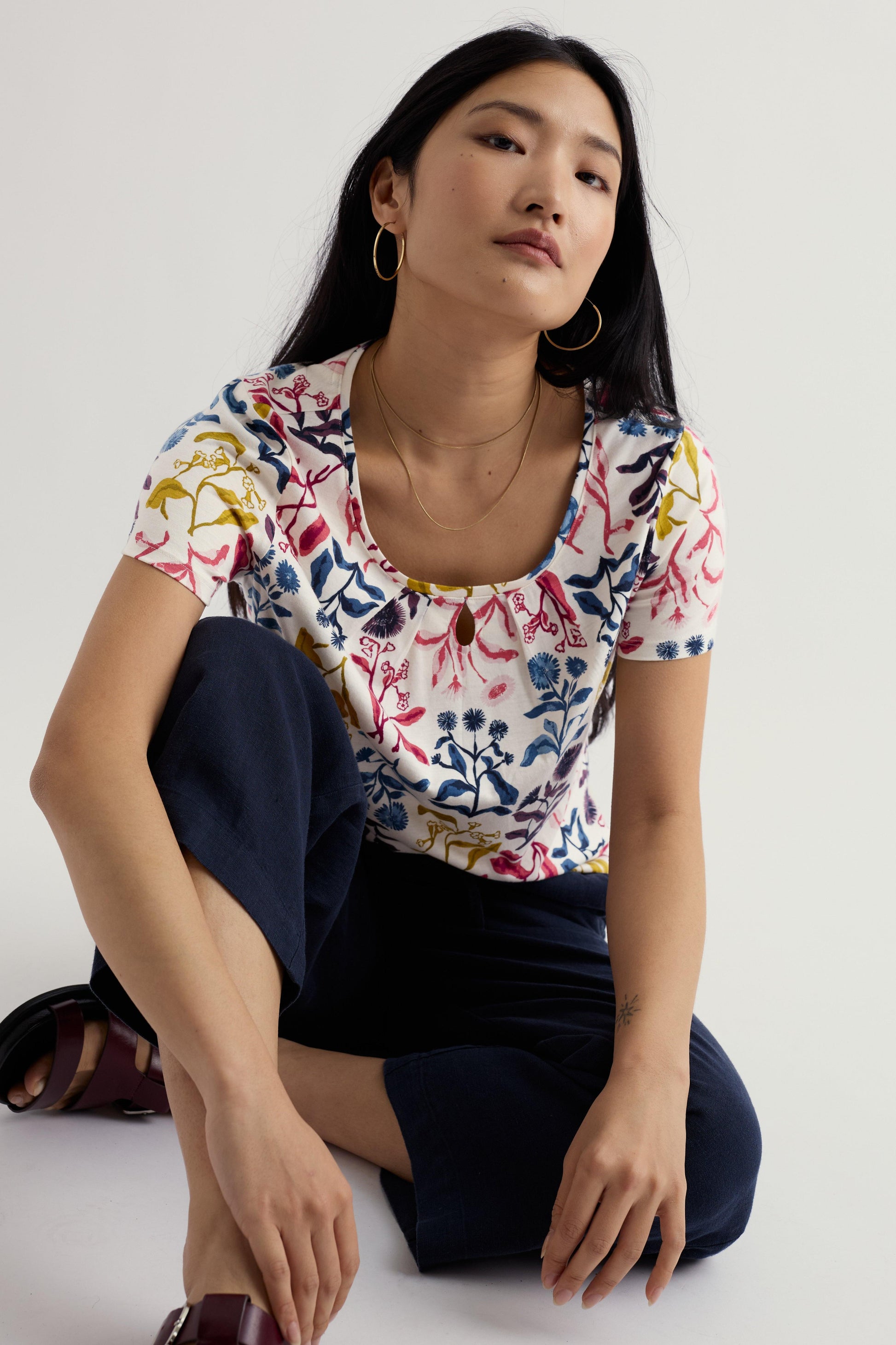 Woman wearing an organi cotton floral-patterned shirt sitting on the floor against a white background