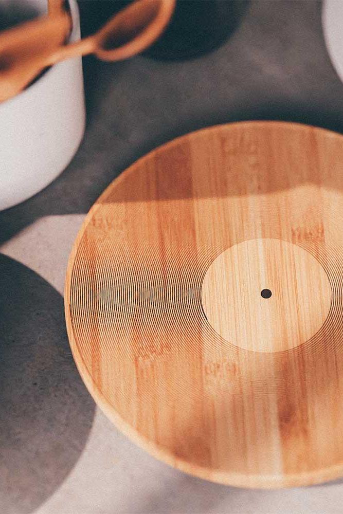 A round bamboo cutting board with a natural wood grain pattern and a lighter circular center, shown on a gray tabletop with partial surrounding kitchen items.