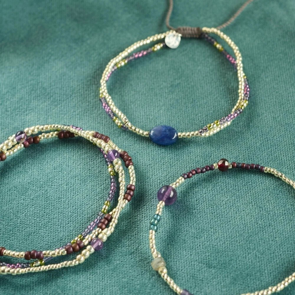 Three handmade beaded bracelets featuring lapis lazuli and other colourful gemstones on a green velvet surface.