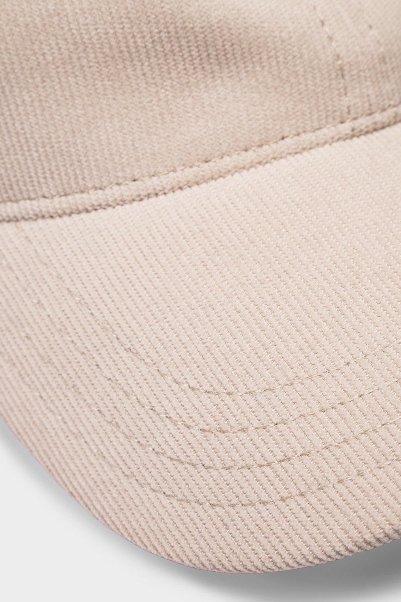 Close-up of a light beige or cream-colored cotton twill baseball cap showing the curved brim and fine fabric texture.