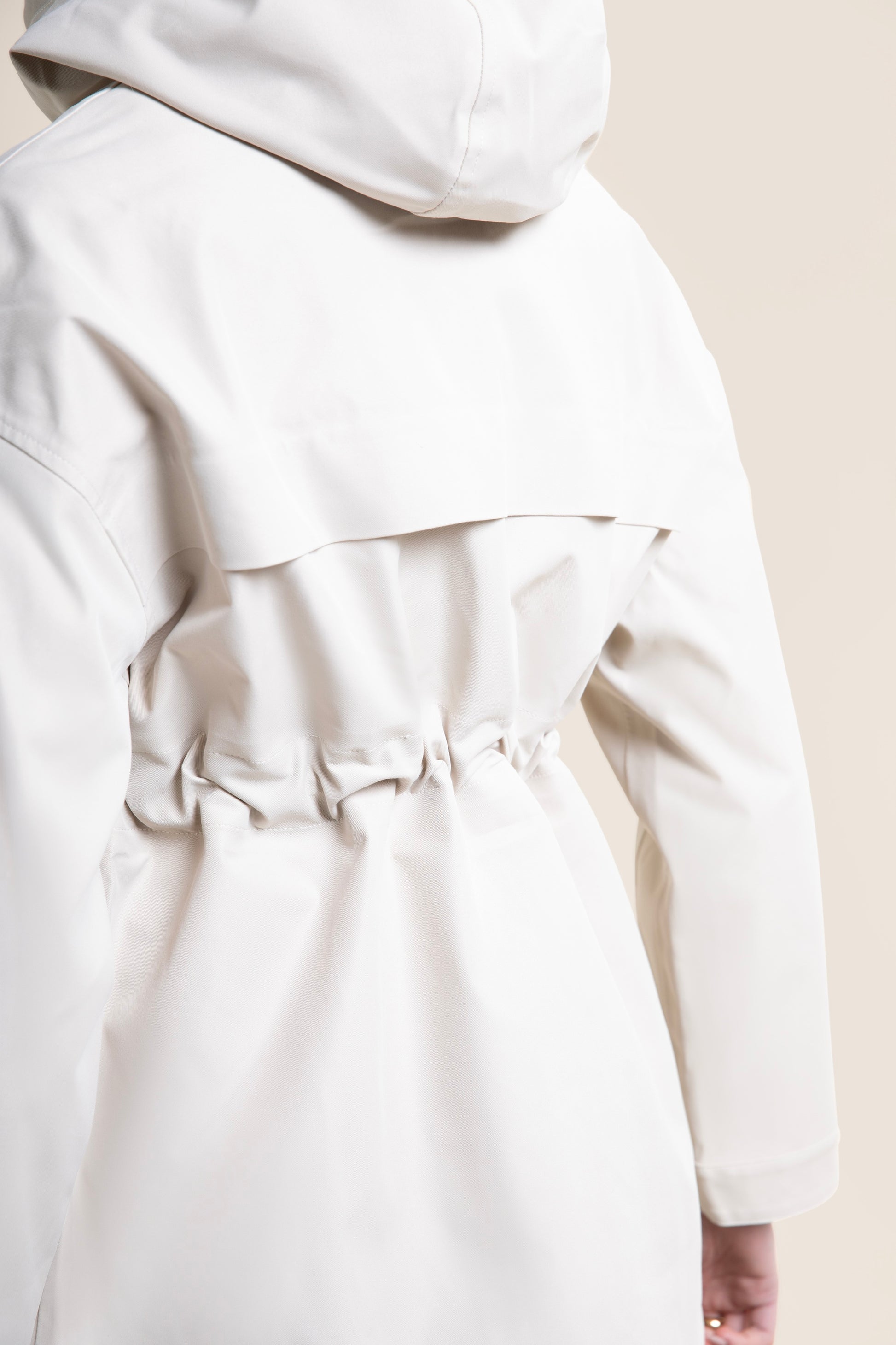Rear view of a person wearing a stylish beige waterproof parka coat with a drawstring waist.