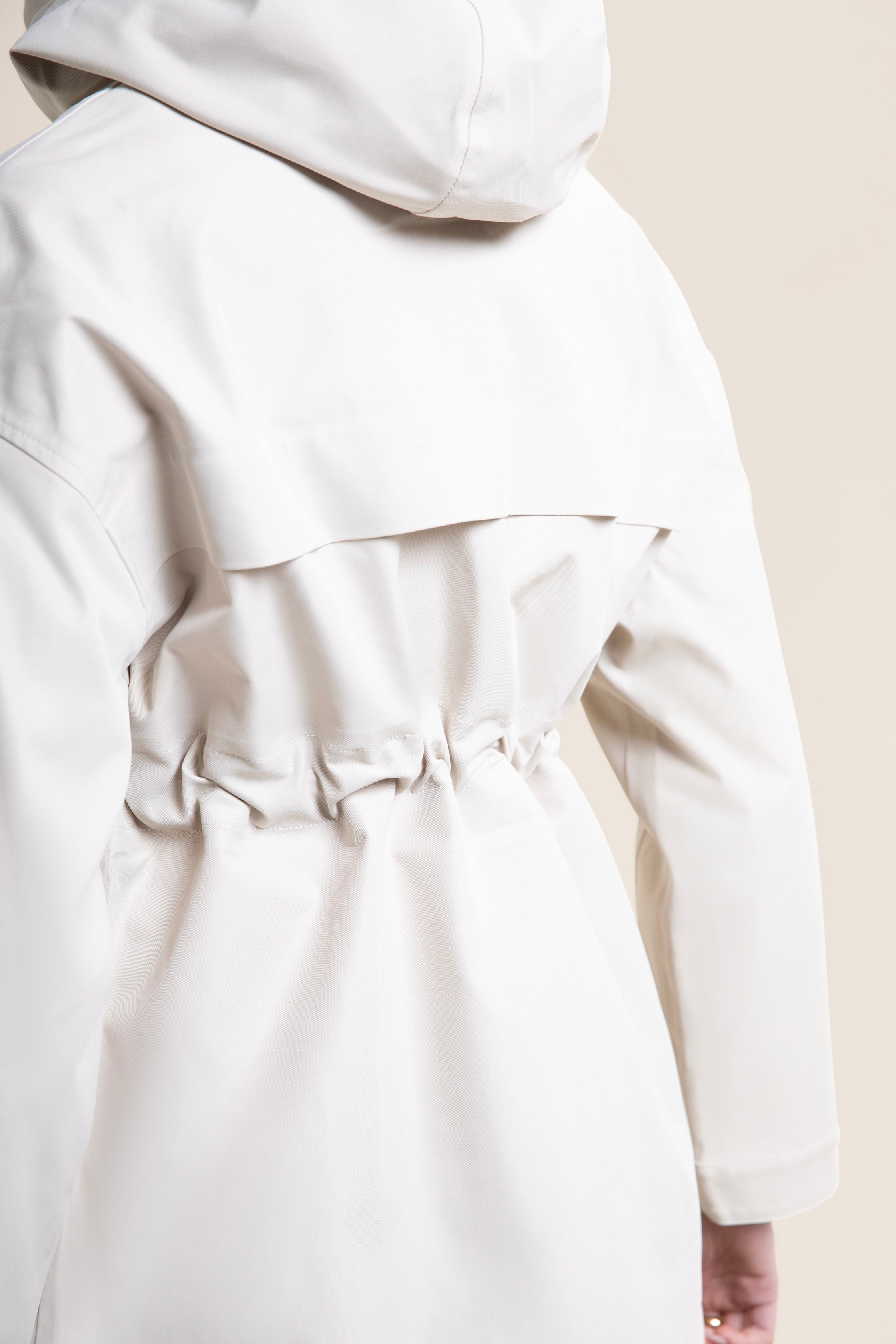 Rear view of a person wearing a stylish beige waterproof parka coat with a drawstring waist.