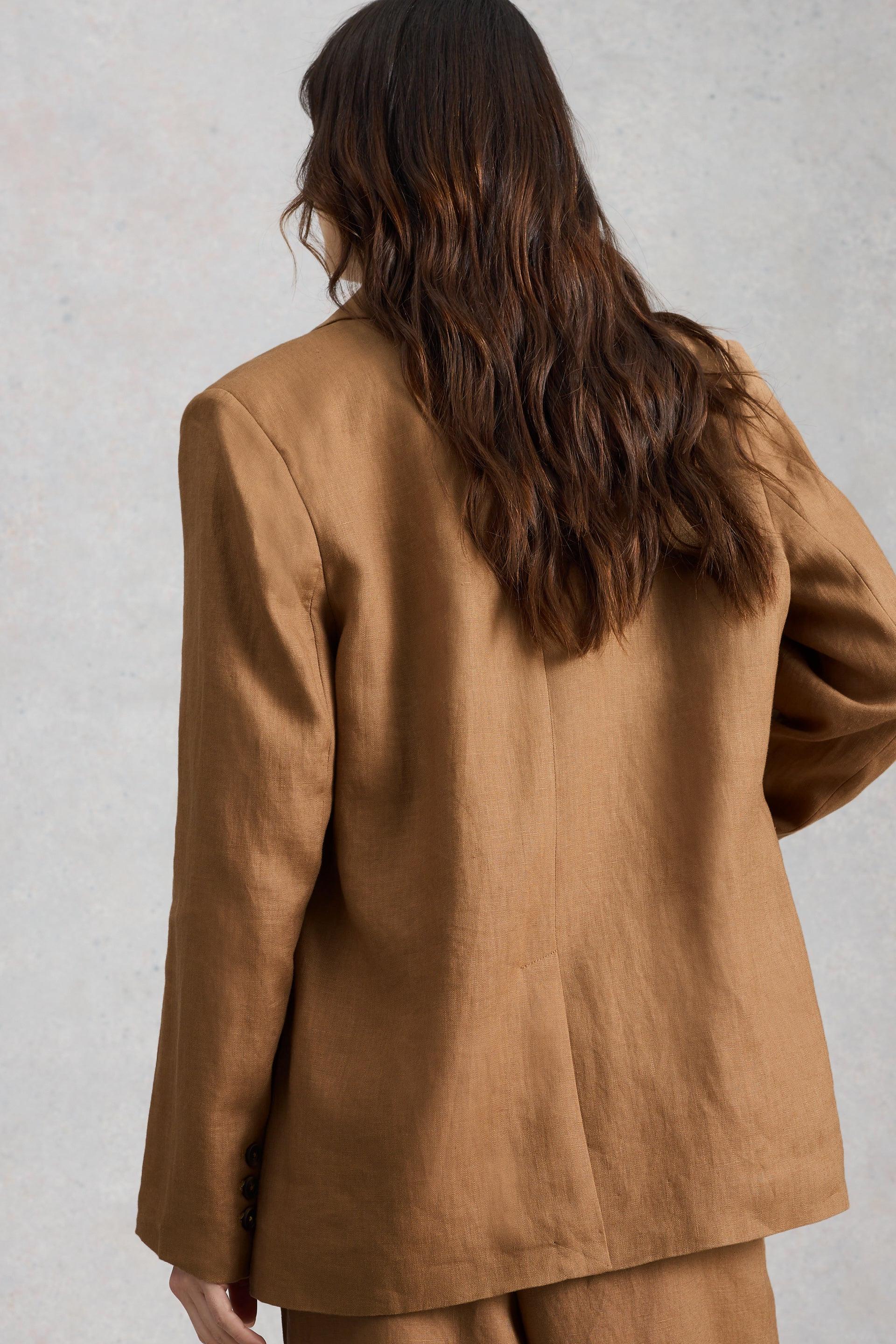 Person wearing a brown oversized linen blazer and matching pants against a plain background