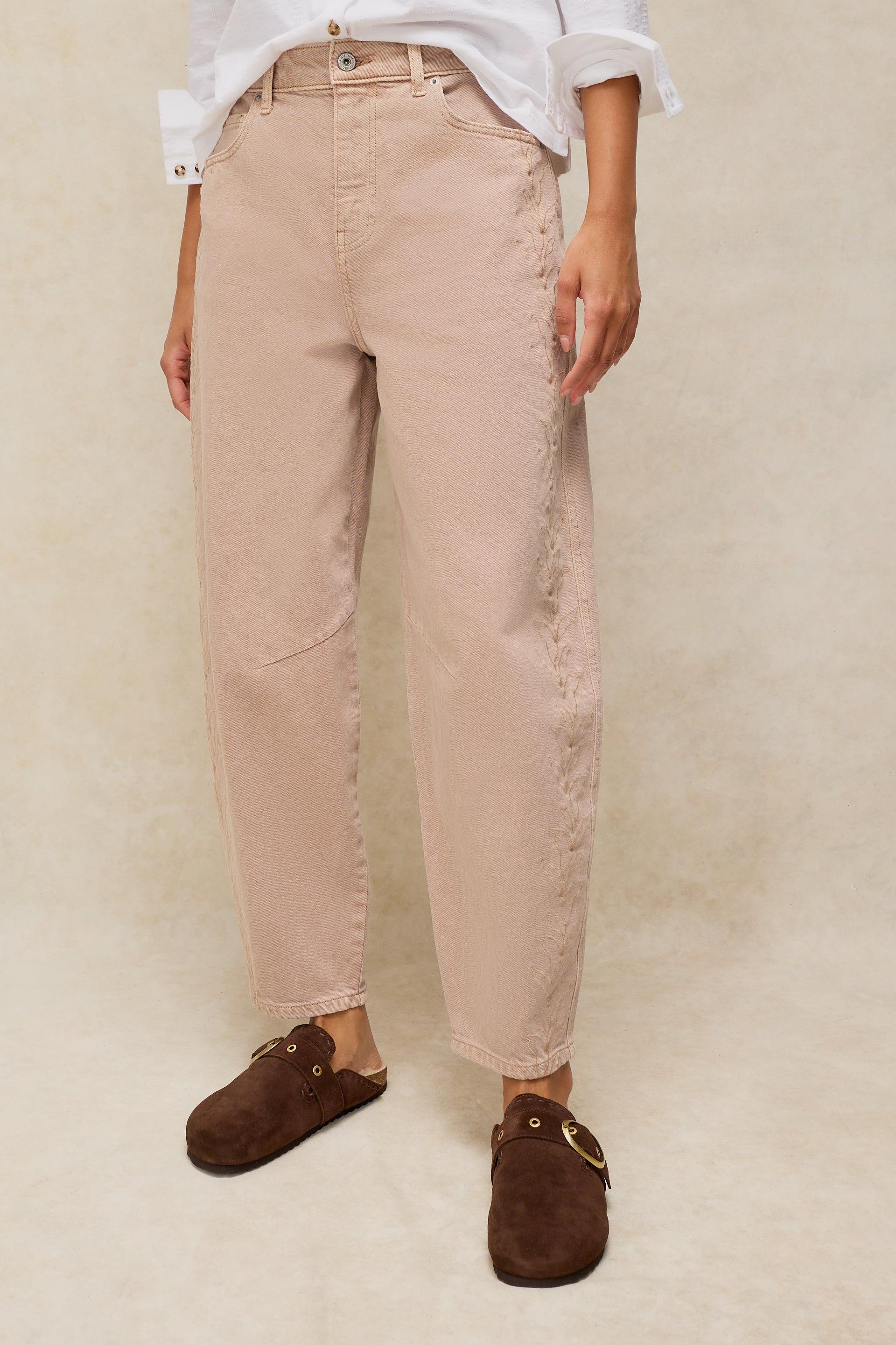 A person wearing beige organic cotton jeans with side embroidery and brown suede mules.