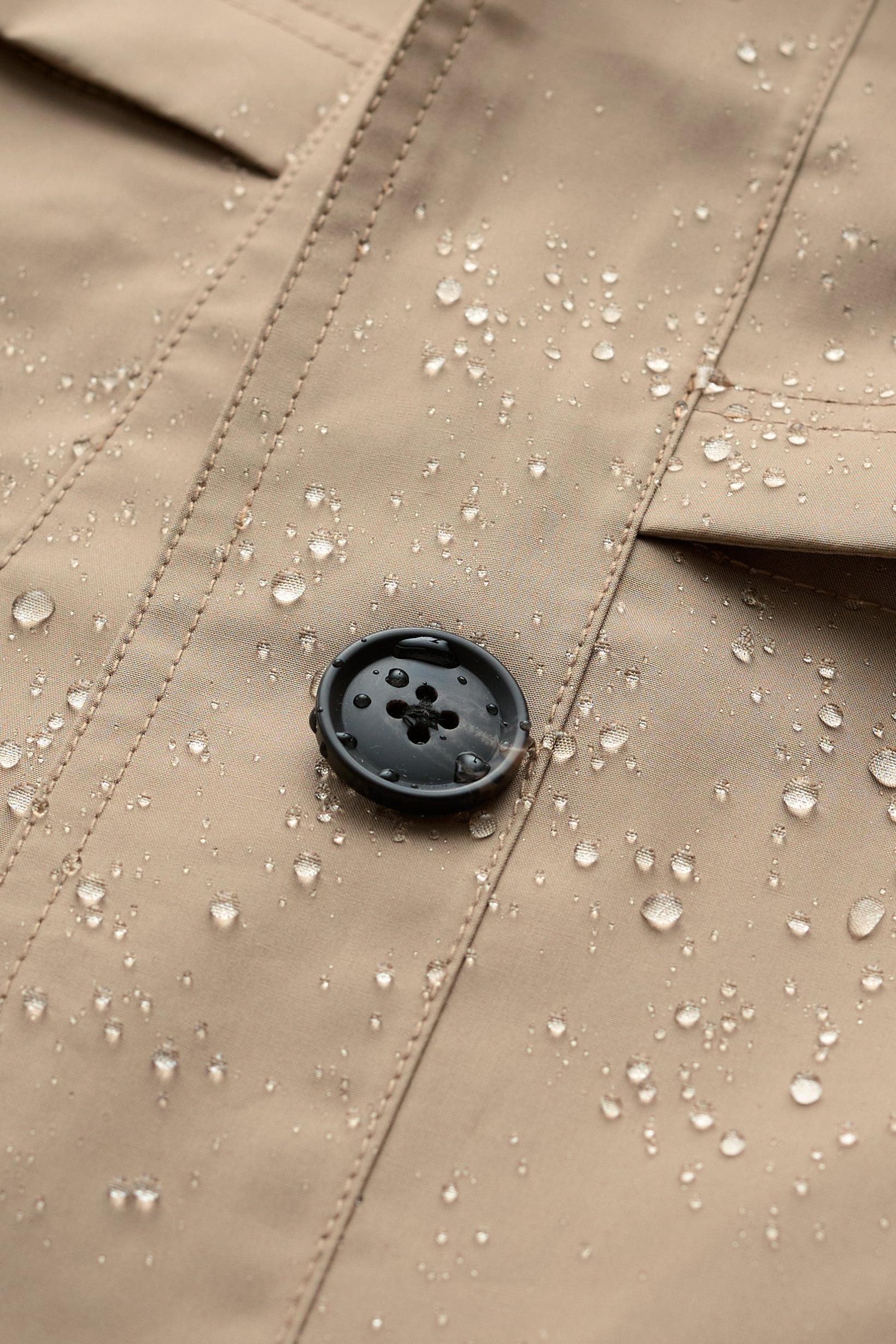 Close-up of a beige waterproof trench coat featuring a black button and scattered clear raindrops.