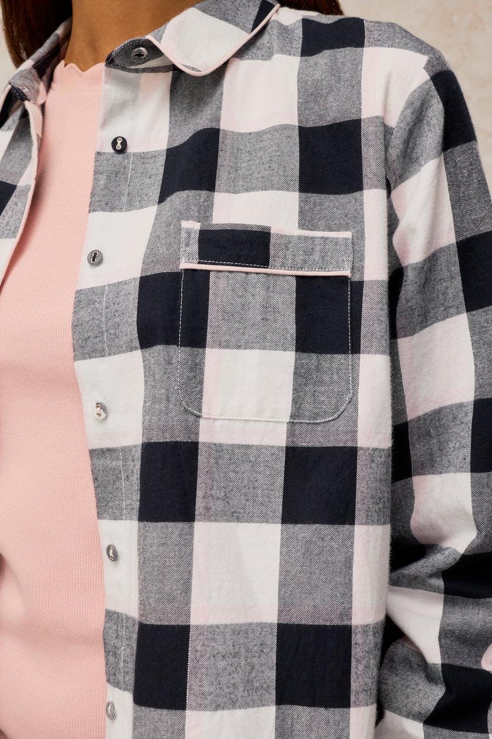 A close-up of a person wearing a cosy black and white check organic cotton pyjama top over a soft pink base layer.